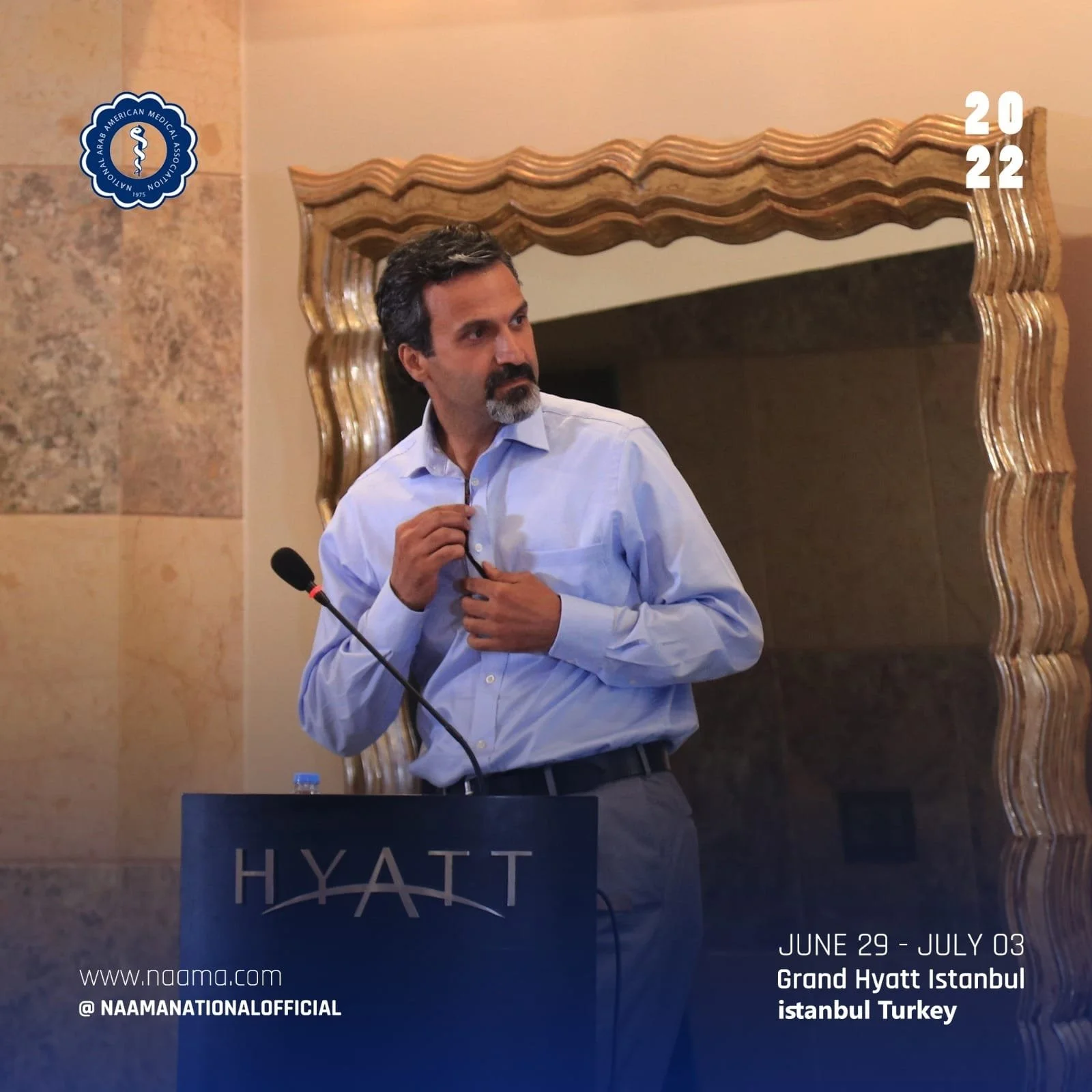 A man with dark hair and a beard wearing a light blue dress shirt, adjusting his collar, standing behind a podium at a conference or event at the Grand Hyatt Istanbul, with a mirror and textured wall in the background. The event dates are June 29 - J