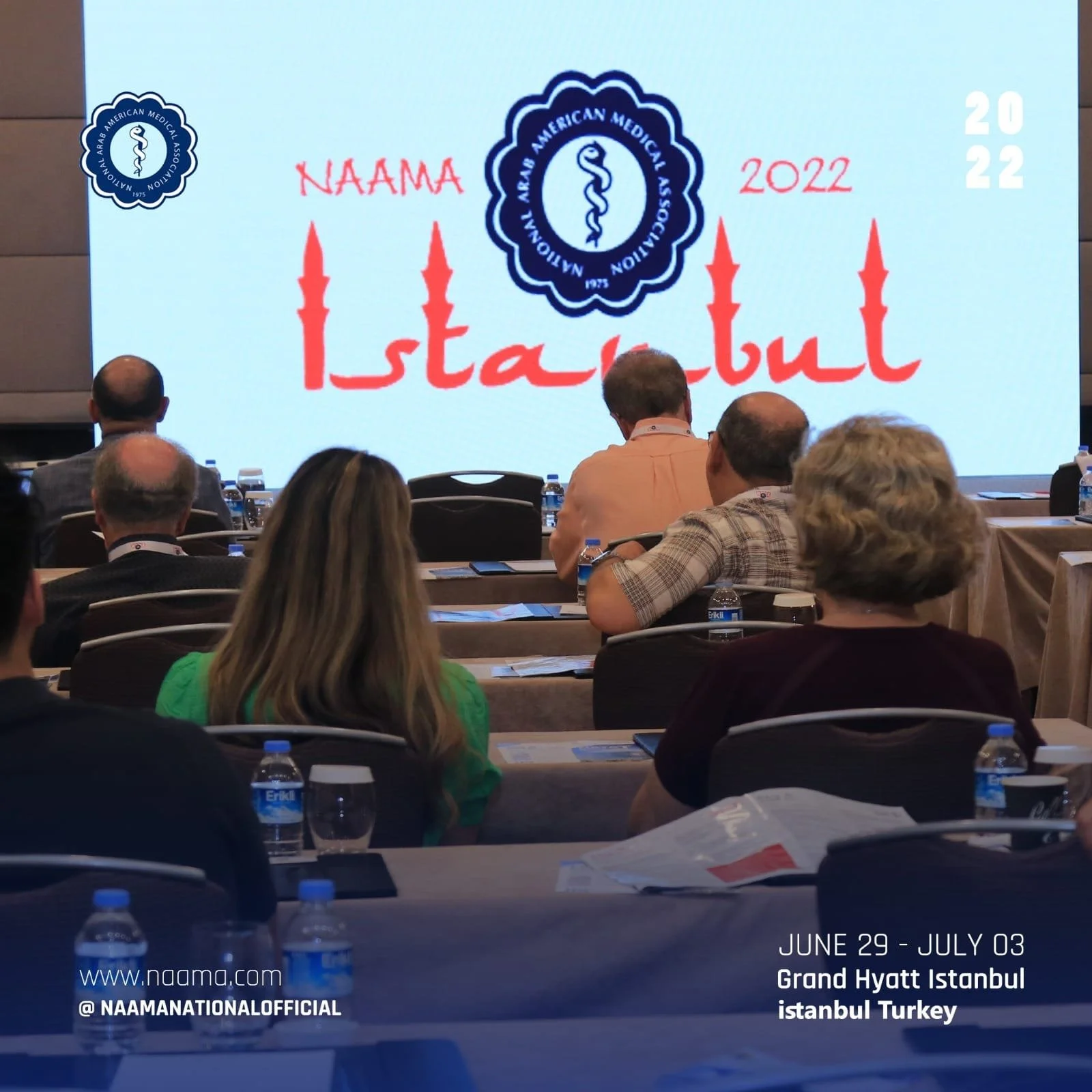 Conference room scene with attendees seated at tables, facing a screen displaying the NAAMA 2022 Istanbul conference logo and details, including dates June 29 to July 3 at the Grand Hyatt Istanbul in Turkey.