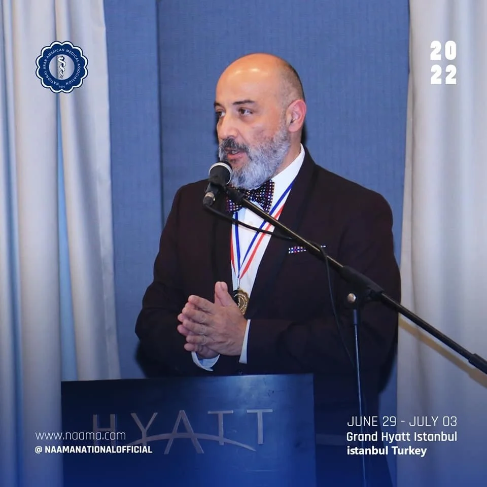 A man with a beard in a suit and bow tie giving a speech at a podium with a microphone. He is wearing medals around his neck. The setting appears to be a conference or award ceremony at the Grand Hyatt in Istanbul, Turkey, from June 29 to July 3, 202