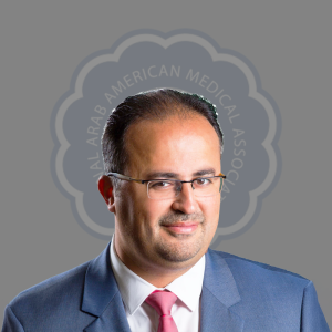 Portrait of a man wearing glasses in a blue suit with a pink tie, smiling, with a medical organization's logo in the background.