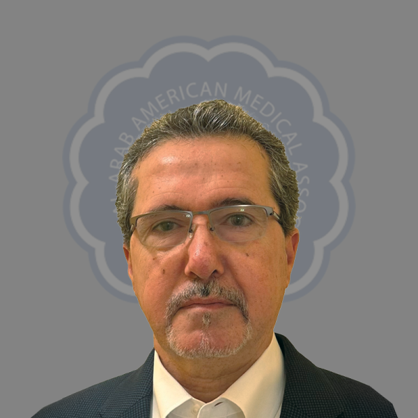 A middle-aged man with gray hair, wearing glasses and a suit, standing in front of a gray background with a logo of the American Medical Association.