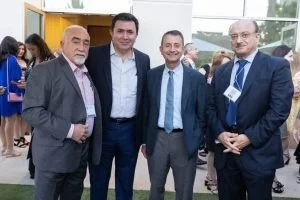 Four men in formal attire posing together outdoors at a professional or social event.