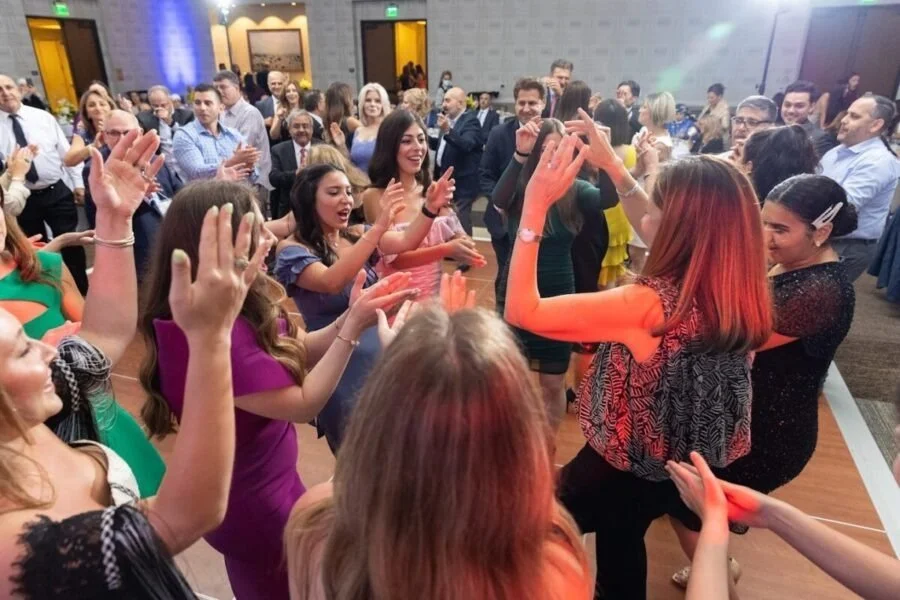 People dancing and celebrating at a lively party or wedding reception in a banquet hall.