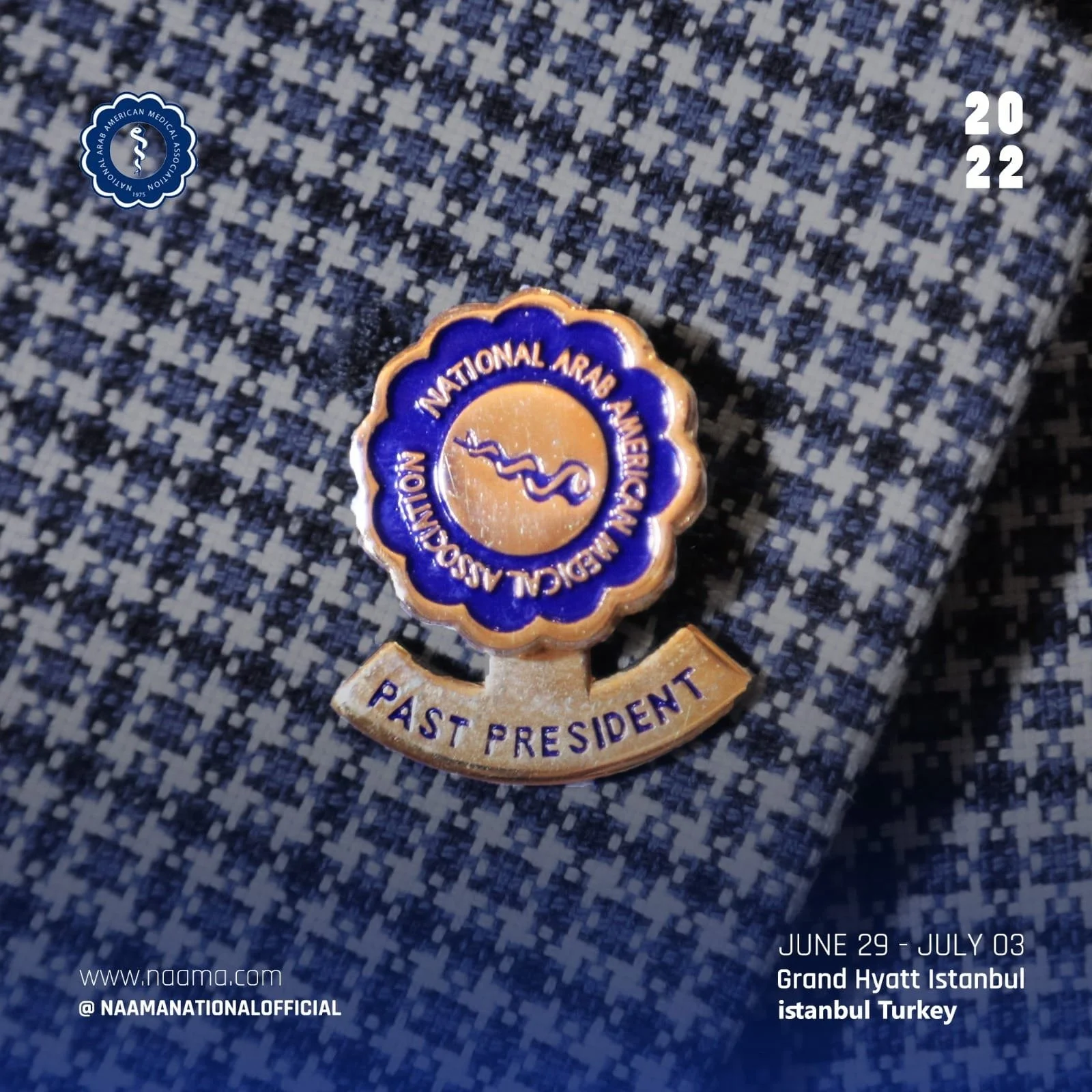 Close-up of a medal pinned to blue and white checkered fabric, with the text 'NAI Saudi Arabia Arab American Medical Association Past President' and the dates 'June 29 - July 03, 2022' at the bottom right, and the logo of the Saudi Arabia Arab Americ