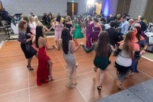 Group of people dancing in a circle at a social event or party in a banquet hall.