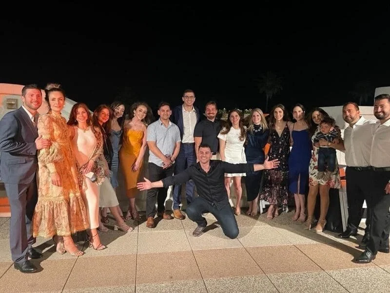 Group of people standing outside at night, posing for a photo with one person squatting in front with arms outstretched.