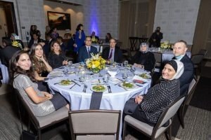 People sitting around a round table at a formal event or banquet, with floral centerpiece and place settings.