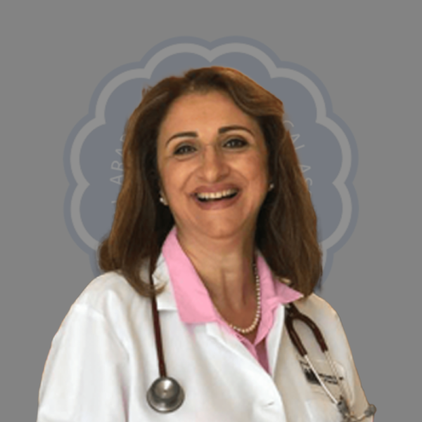 A female doctor smiling, wearing a white coat, pink shirt, pearl necklace, and stethoscope, with a medical emblem in the background.