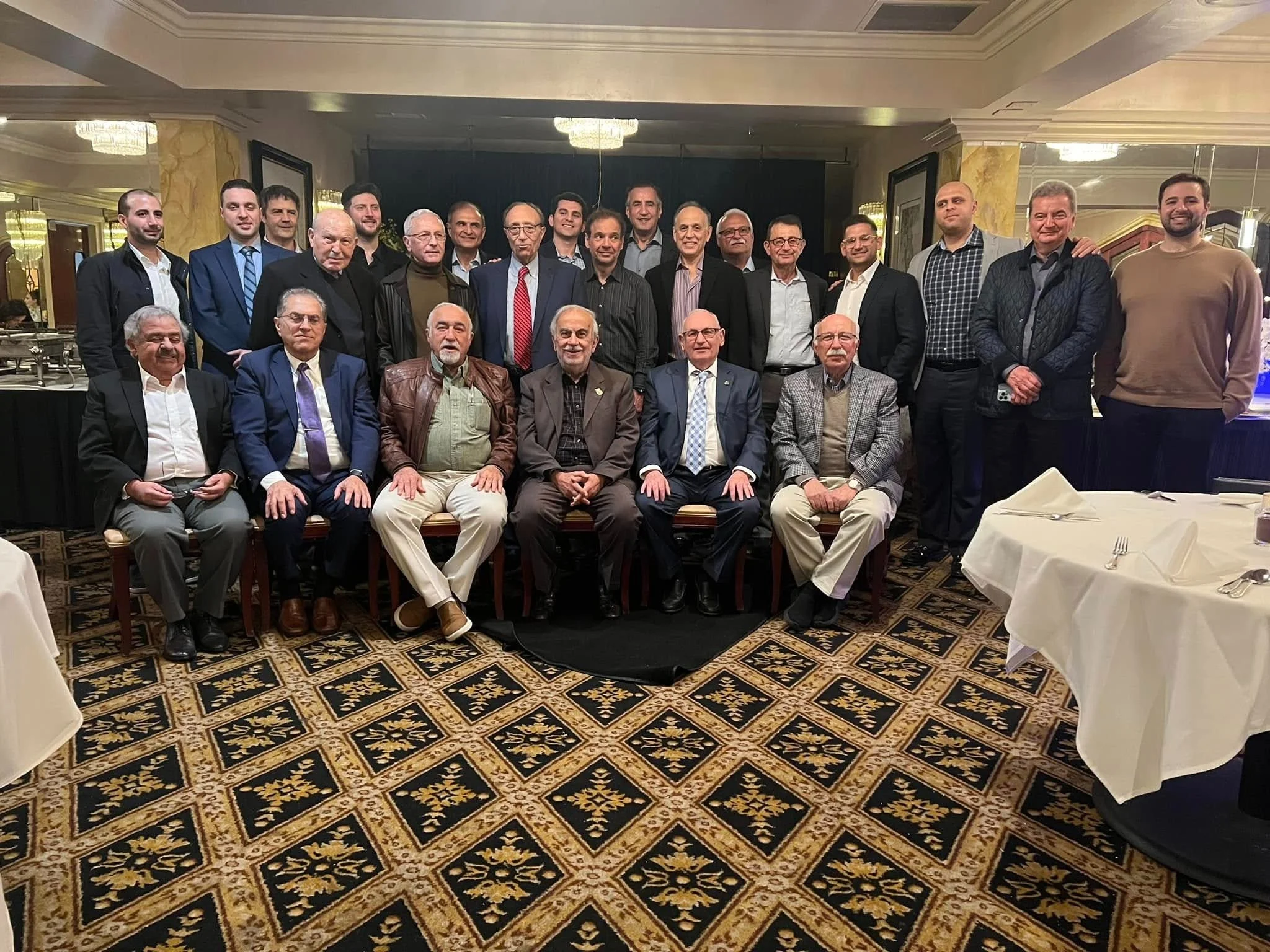 Group of men seated and standing in a formal dining room for a group photo.