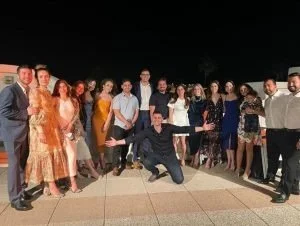 Group of well-dressed people posing together outdoors at night, some smiling and others striking playful poses.