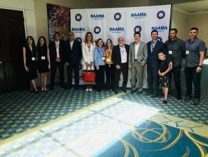 Group of eleven people standing together in front of a NAMA backdrop inside a conference room.