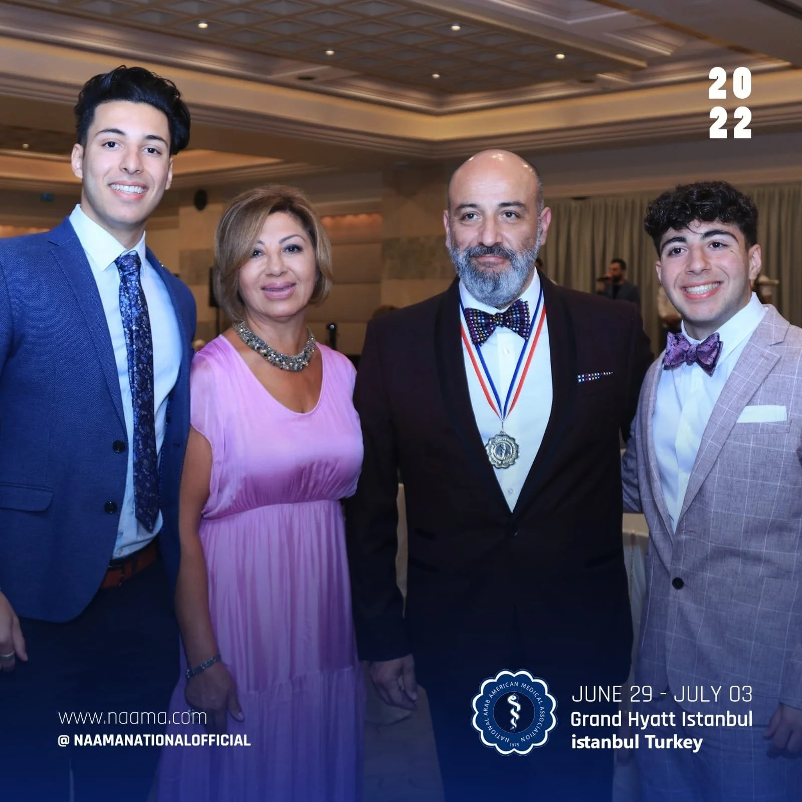 A group of four people dressed formally, standing close together and smiling at the camera, in an indoor setting with a decorated ceiling. The event is at the Grand Hyatt Istanbul, Turkey, from June 29 to July 3, 2022, organized by the Arab American 