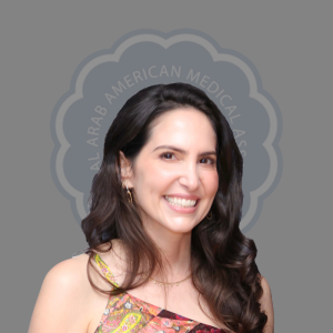 A smiling woman with long dark hair wearing a colorful top, standing in front of a gray background with the words 'Arab American Medical' partially visible.