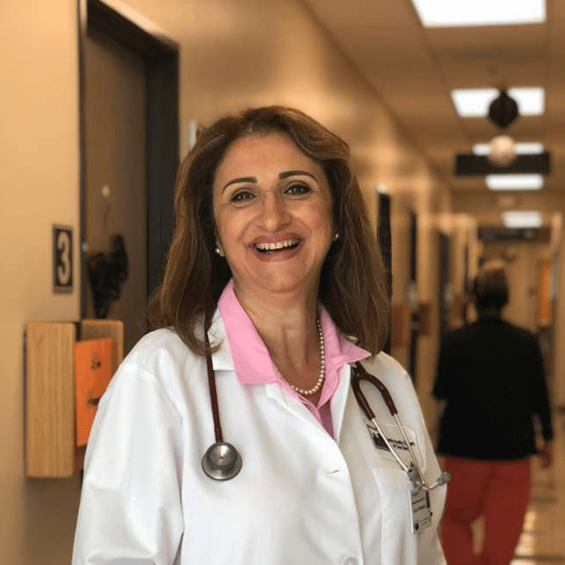A smiley female doctor in a white coat with a stethoscope in a hospital corridor.