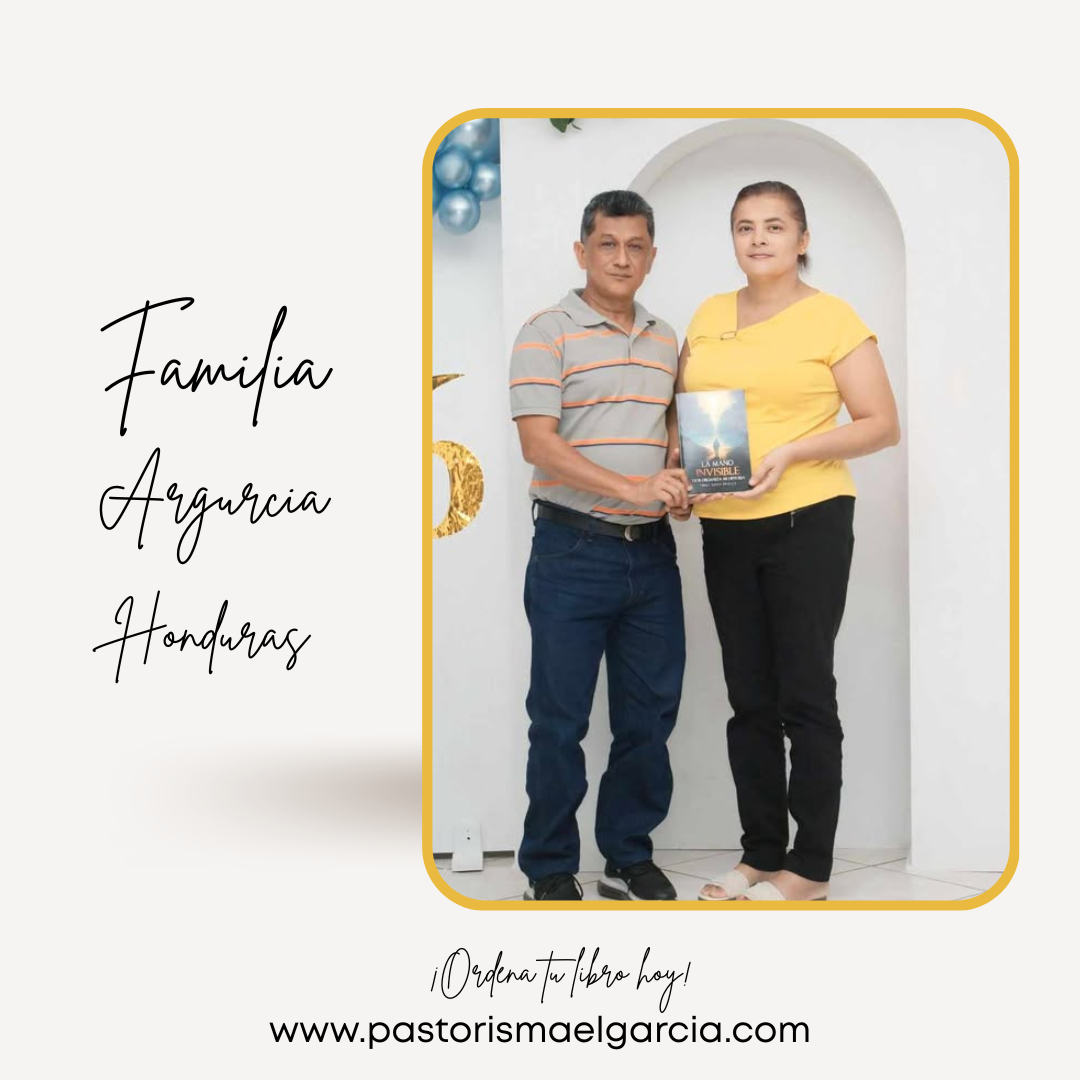 Una pareja de adultos, hombre y mujer, de pie juntos en un entorno interior con fondo blanco y decoraciones en azul y dorado. La mujer sostiene un libro titulado 'En la mano Invisible' y ambos miran a la cámara.