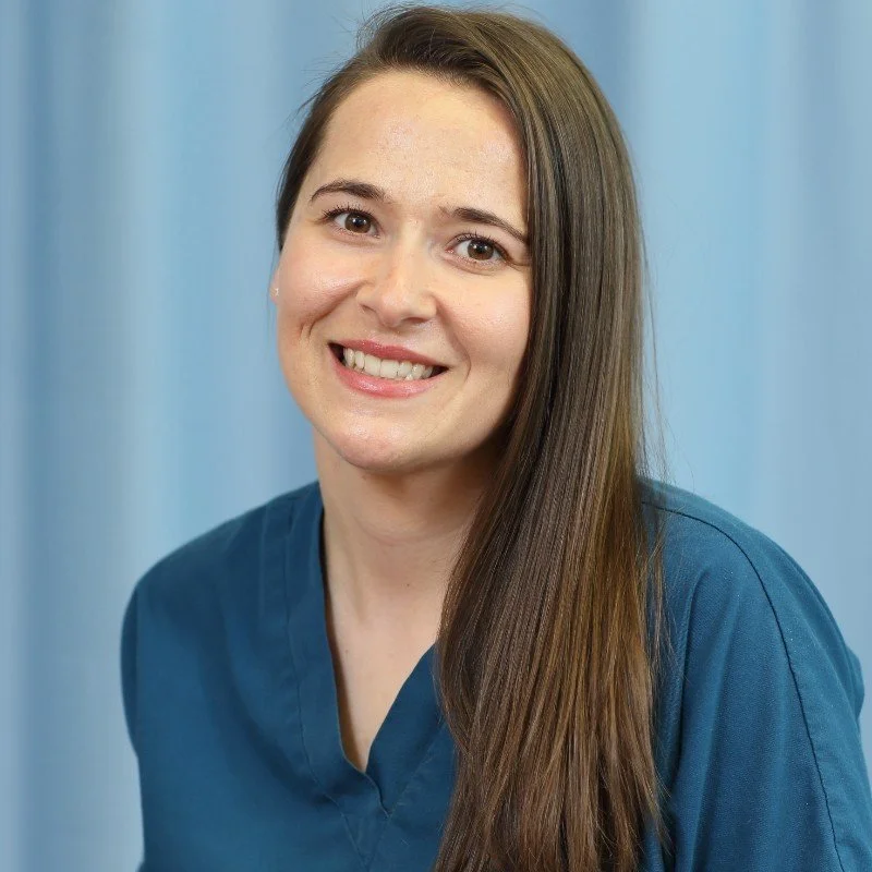 A smiling woman with long brown hair in a dark blue uniform against a light blue background.