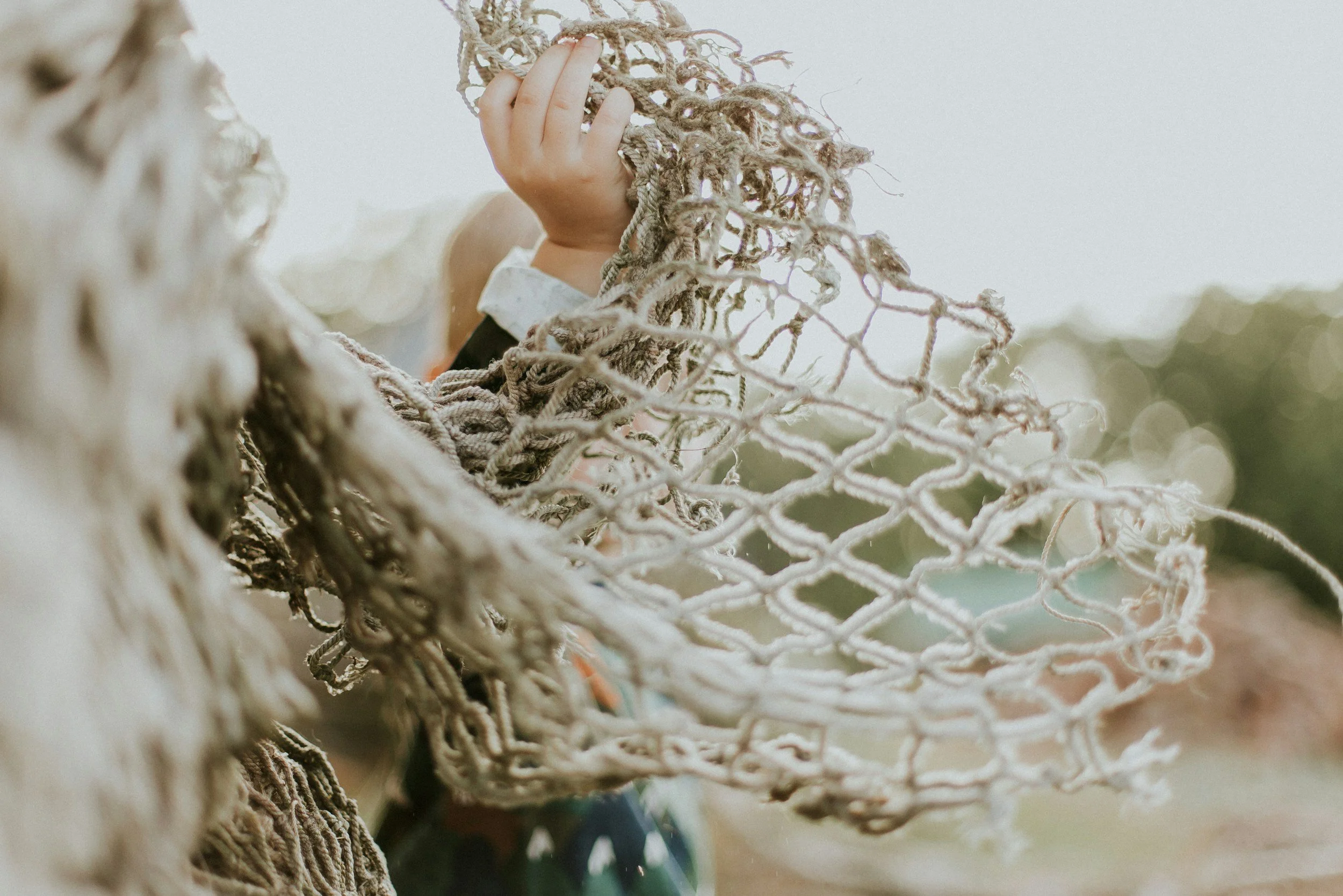 Close-up of a hand holding a tangled, worn soccer net with blurry background.