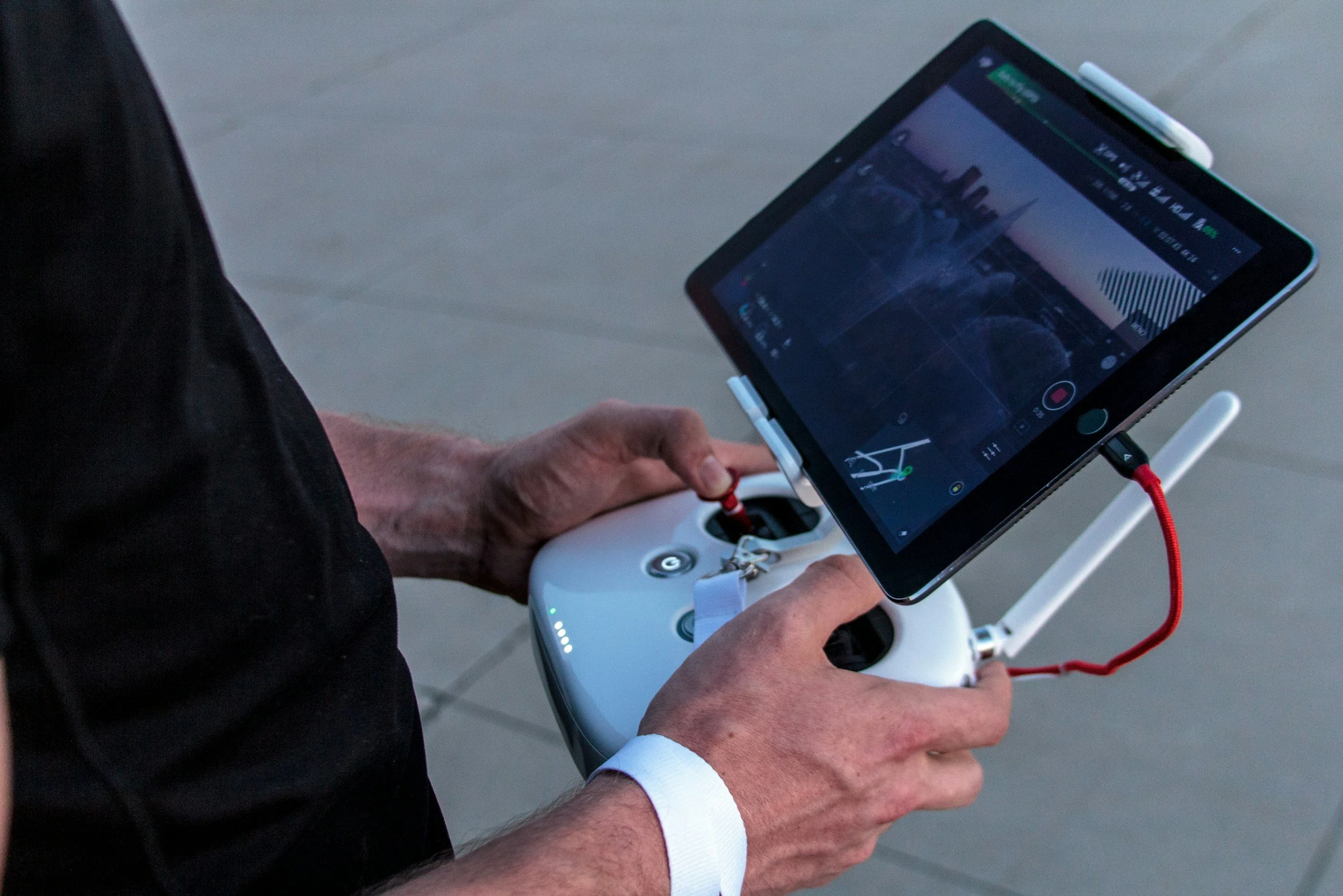 A person operating a drone using a remote controller with a tablet mounted on top, possibly flying the drone.