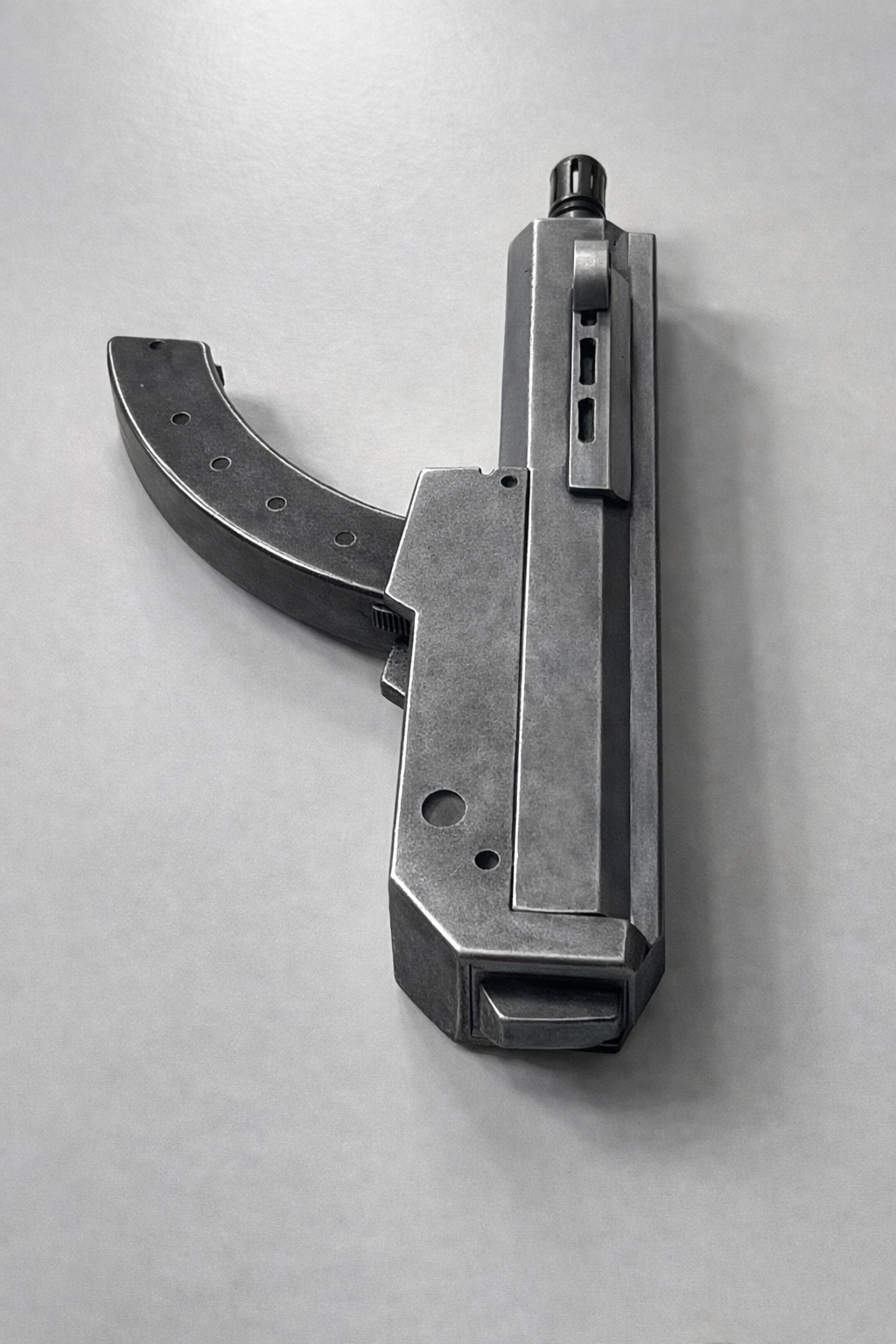 A metallic semi-automatic pistol with a curved magazine lying on a plain light gray surface.
