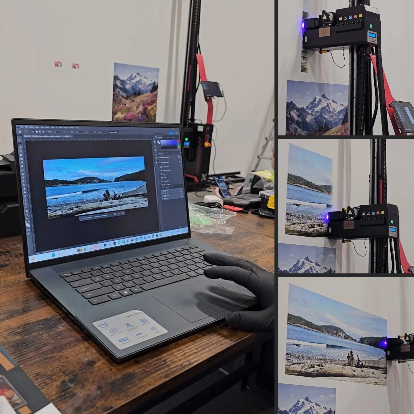 A person wearing a black glove using a laptop on a wooden table, with a print of a landscape photo on the laptop screen. To the right, a large-format printer is printing landscape photographs of mountains and coastal scenes, mounted on a white wall.