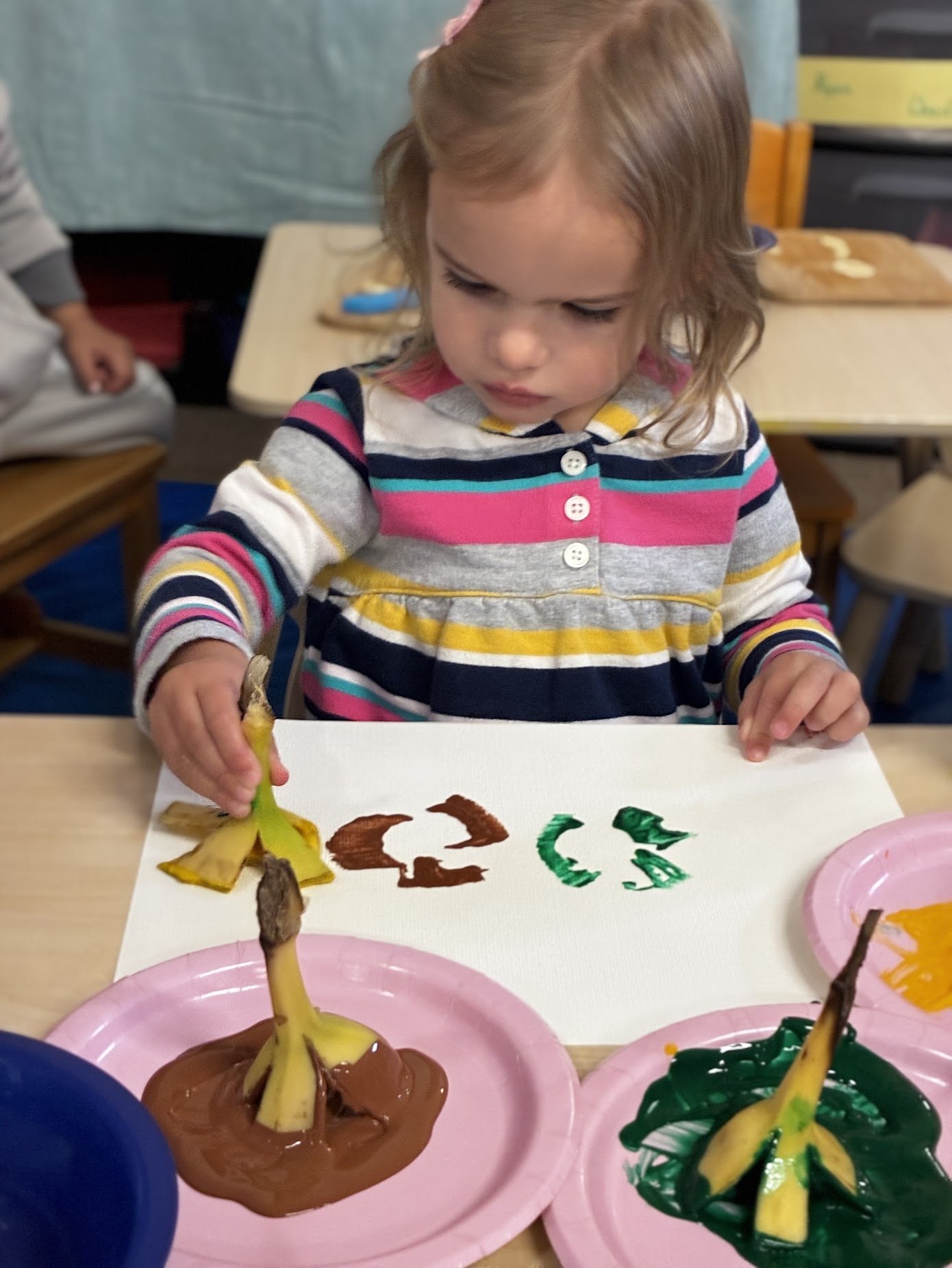 young toddler practicing process art and using a banana to paint