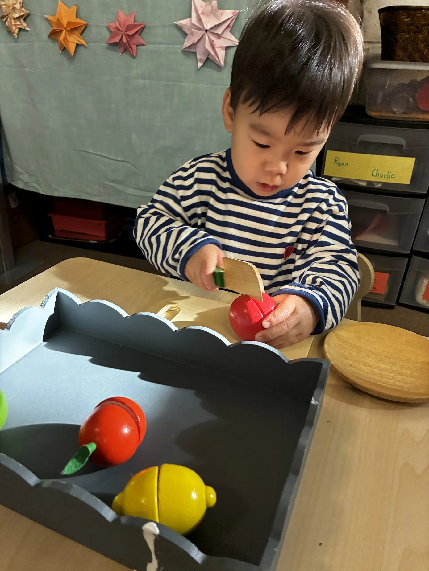 young toddler practicing cutting wooden fruit with a wooden knife