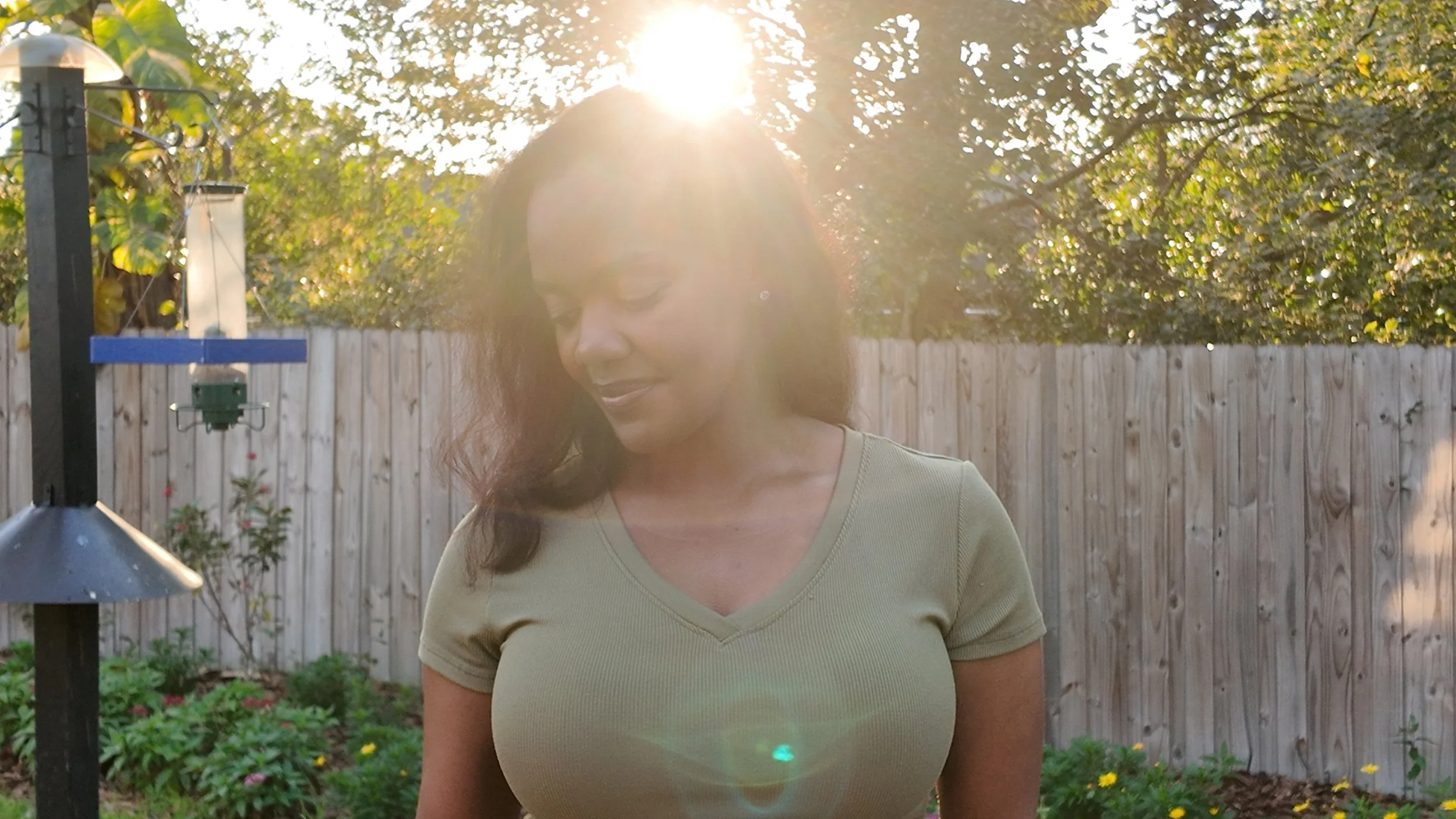 Courtney standing in her backyard garden near bird feeders during golden hour sunlight.