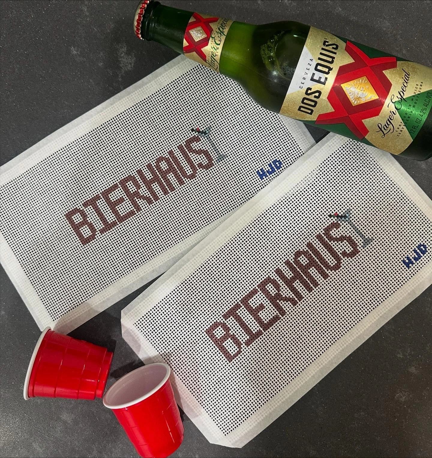 Two perforated sheets with the words 'Biergarten' and 'Hof' printed on them, a bottle of Dos Equis beer, and two empty red plastic cups.