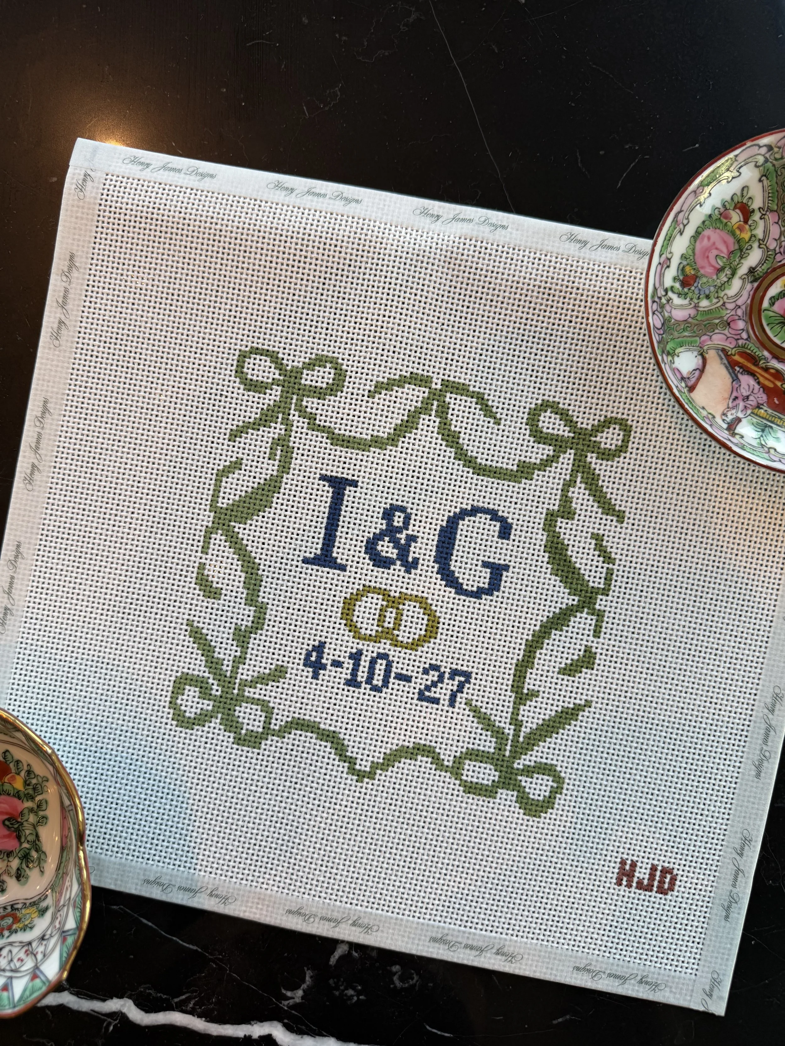 Cross-stitch pattern on fabric with a green ribbon design, the word 'Tea', and the date '4-10-27', partially visible, surrounded by decorative border.