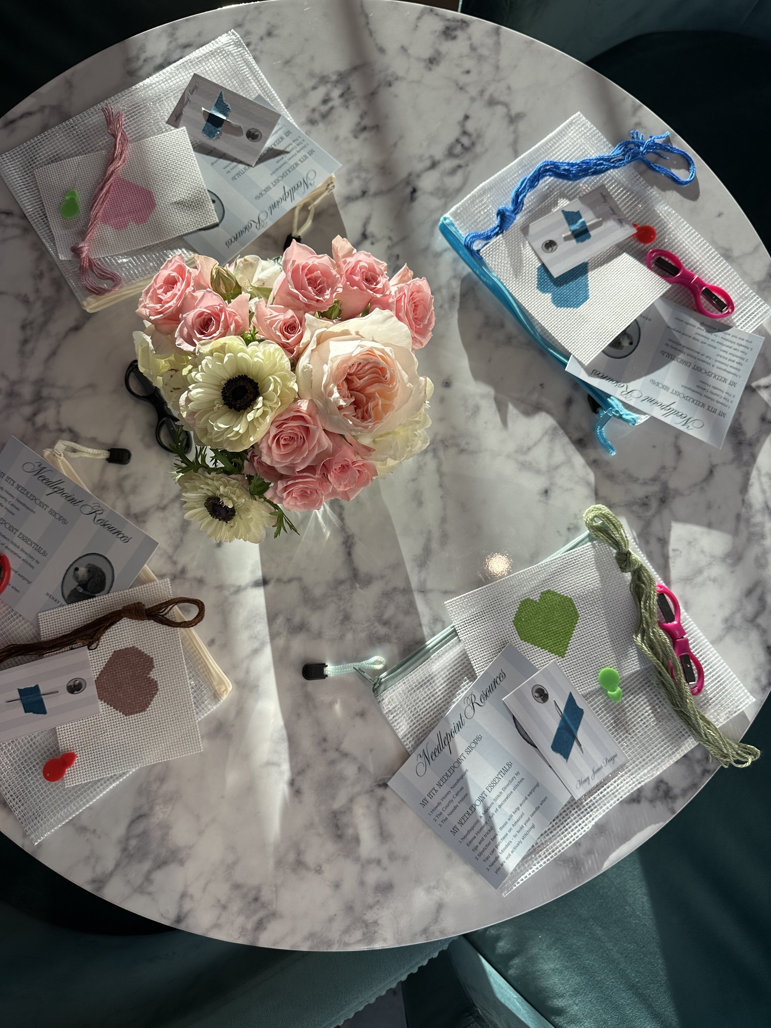 A marble table with various small crafting kits, a bouquet of pink and white roses, and a few sheets of paper with text and images.
