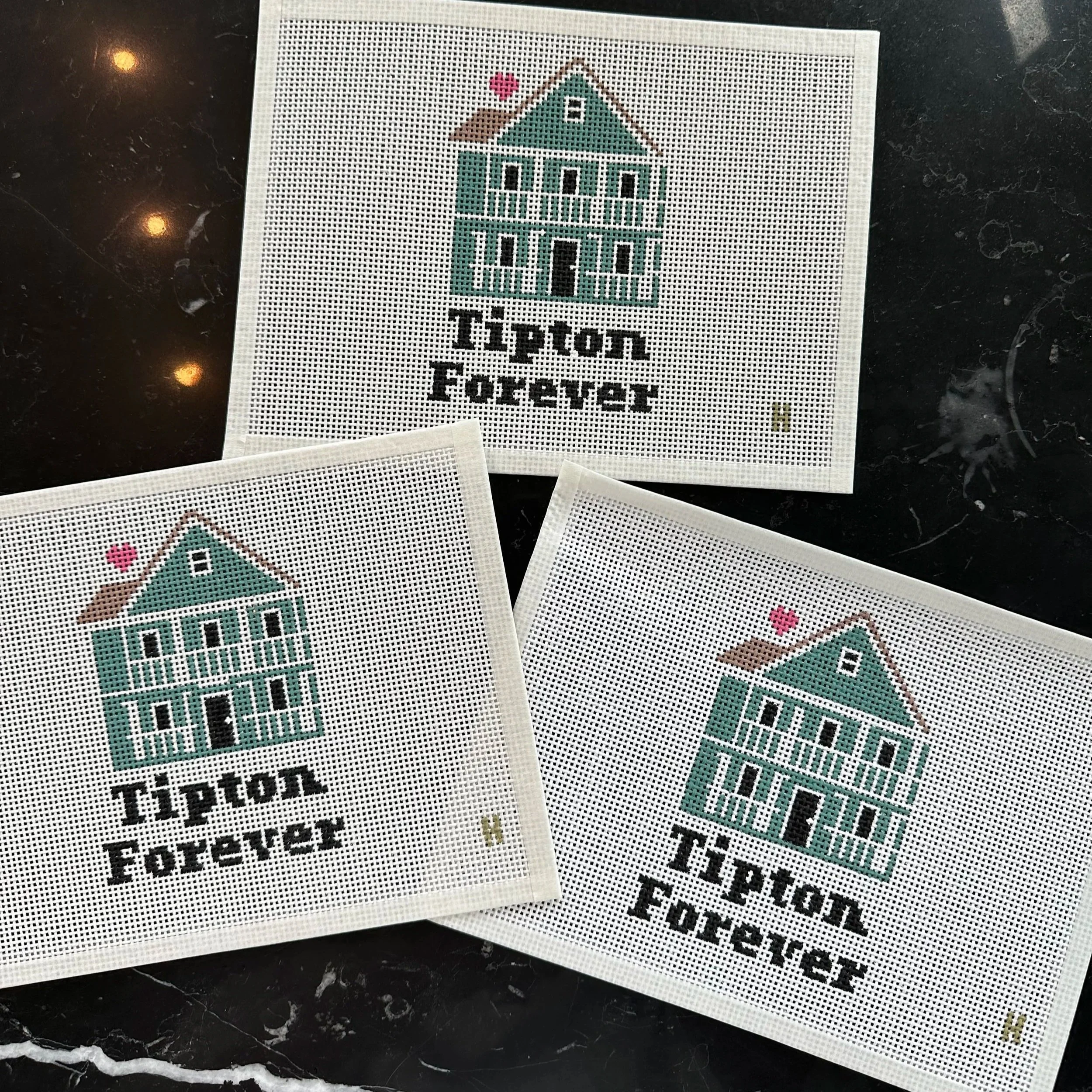 Cross-stitch hoop with a house design and the text 'Home Forever' on white fabric, placed on a black marble surface.