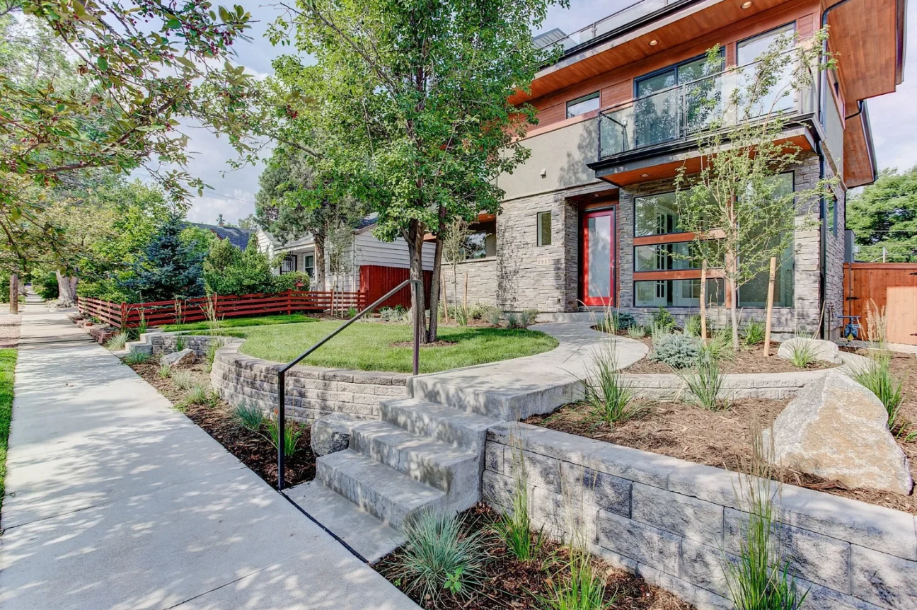A modern Sloan duplex home with cedar siding, native landscaping, and a red front door on a quiet Denver street