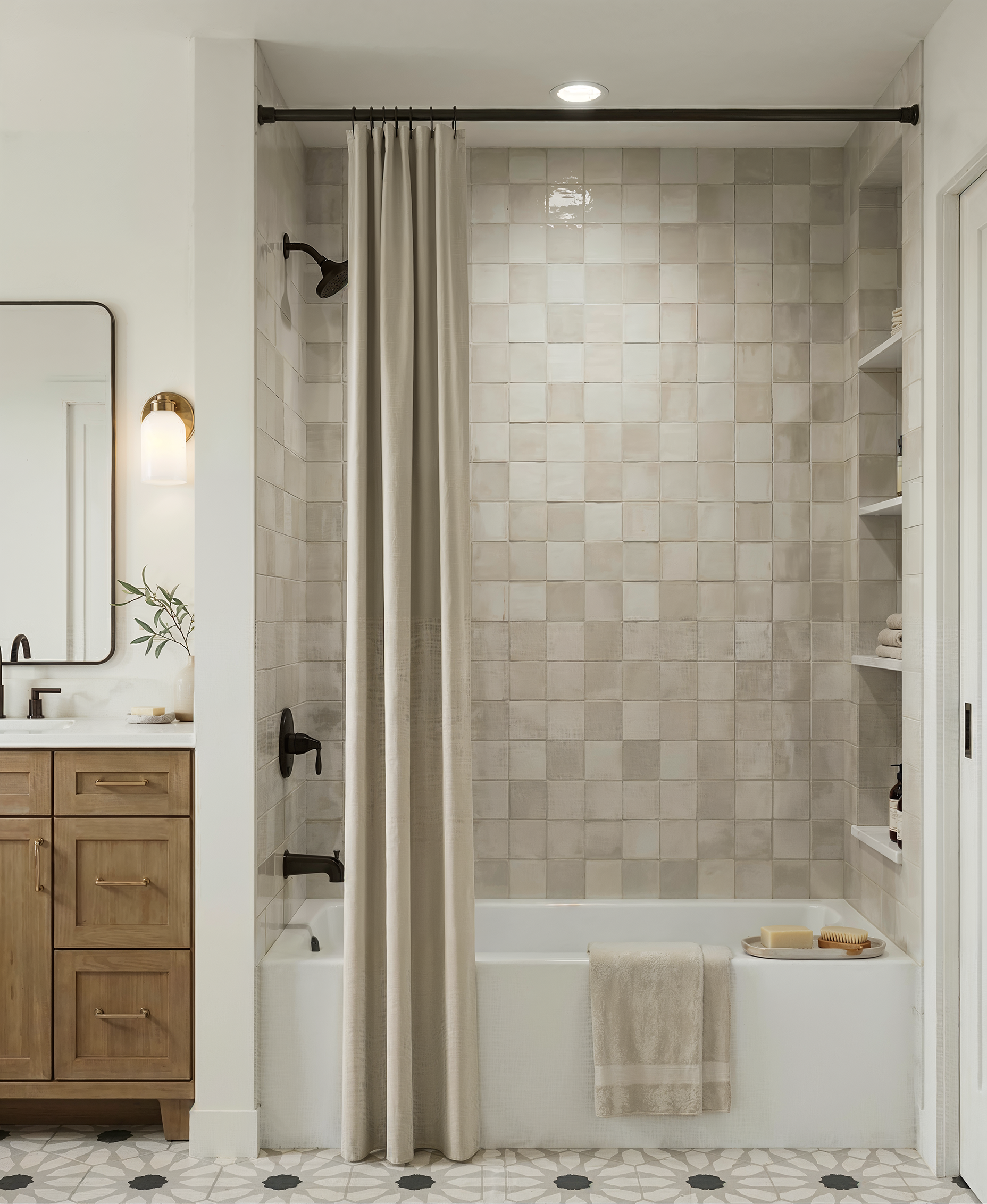 A secondary bathroom in the Julian Street duplex, with a wood vanity, black fixtures, a tub and shower wrapped in hand-glazed square tile, a built-in niche, and a patterned mosaic floor.