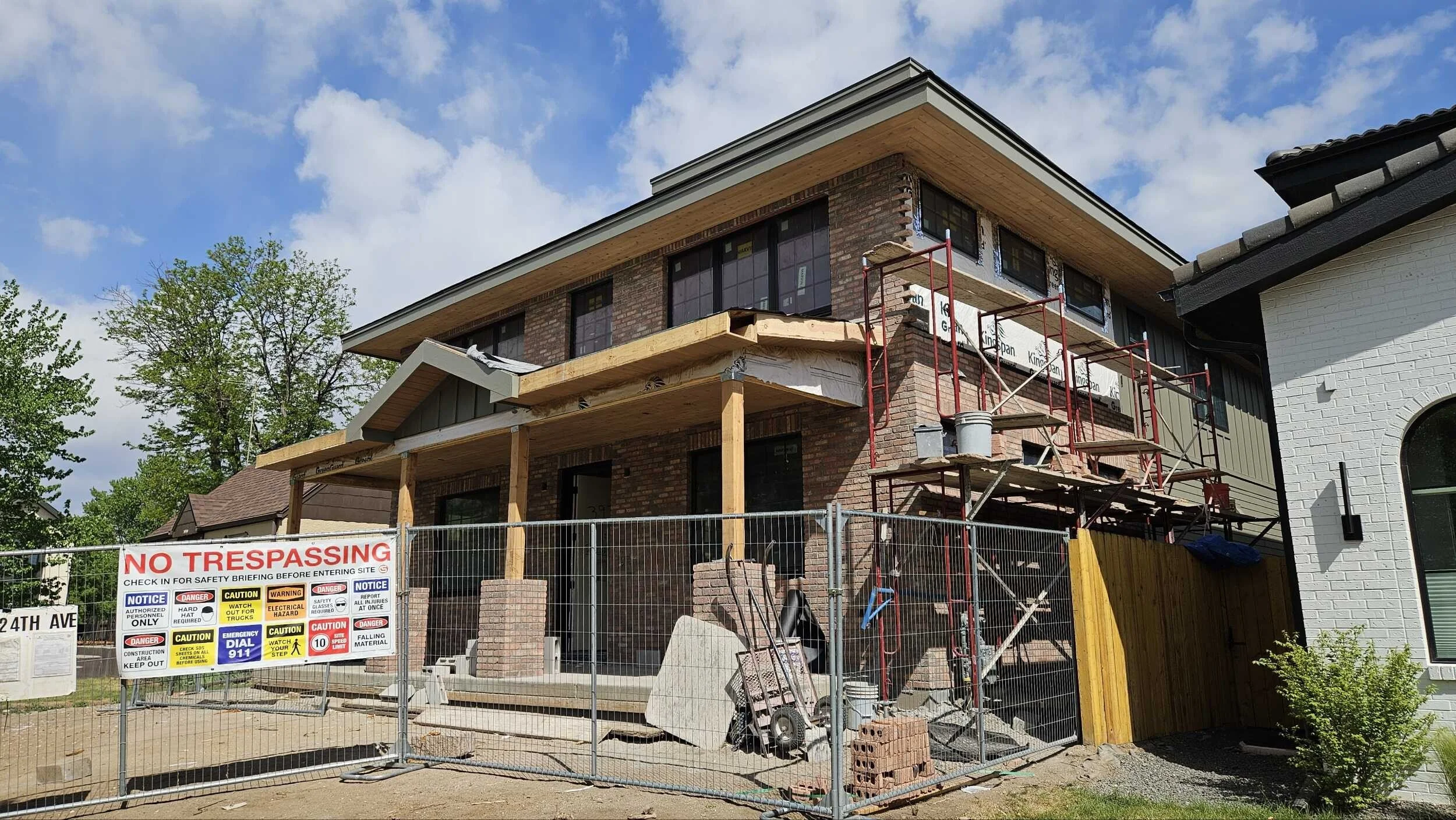 Under construction house with scaffolding, construction signs, and a wooden porch being built, surrounded by a temporary fence.