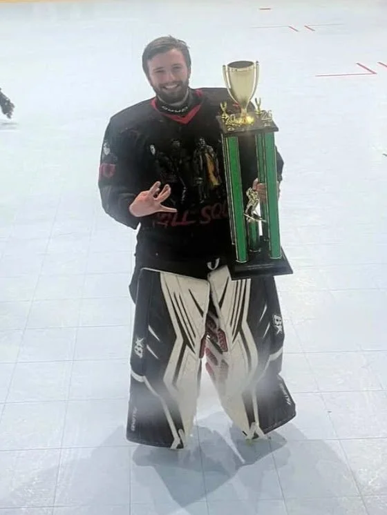A person wearing hockey gear holding a large trophy on an ice rink.