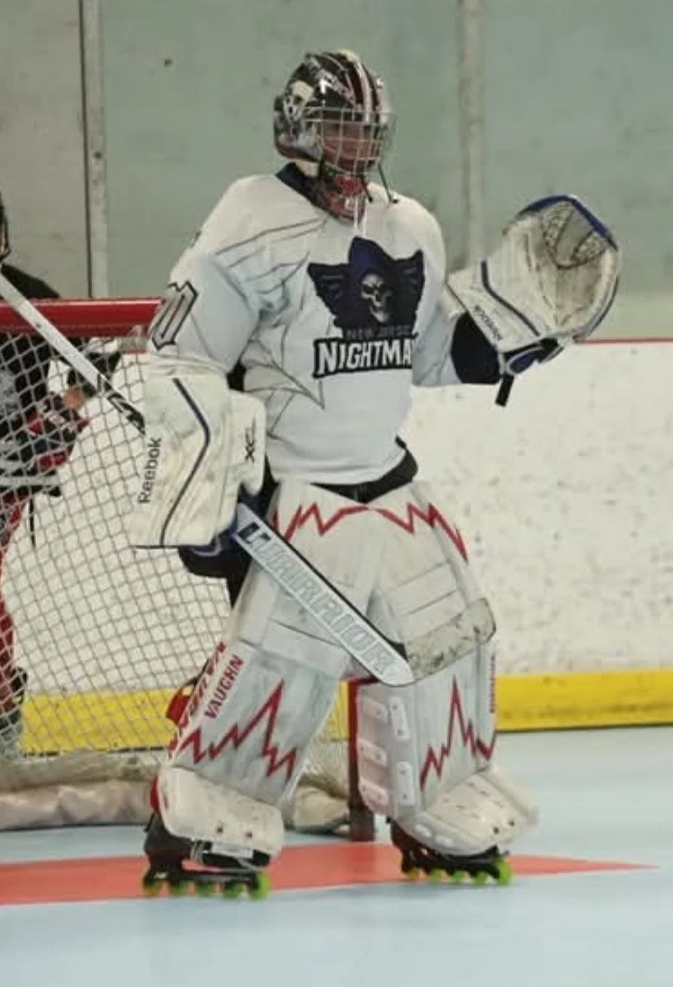 Ice hockey goalie in white and red gear standing in front of the net during a game.