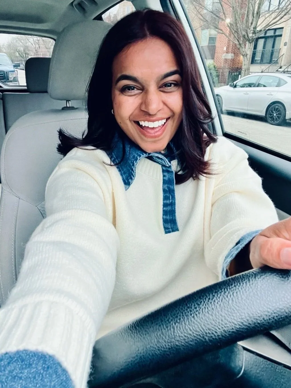 Sarah Corley smiling in the driver's seat of a car wearing a cream sweater with a denim collar featured on the Take Your Vitamins thank you page.