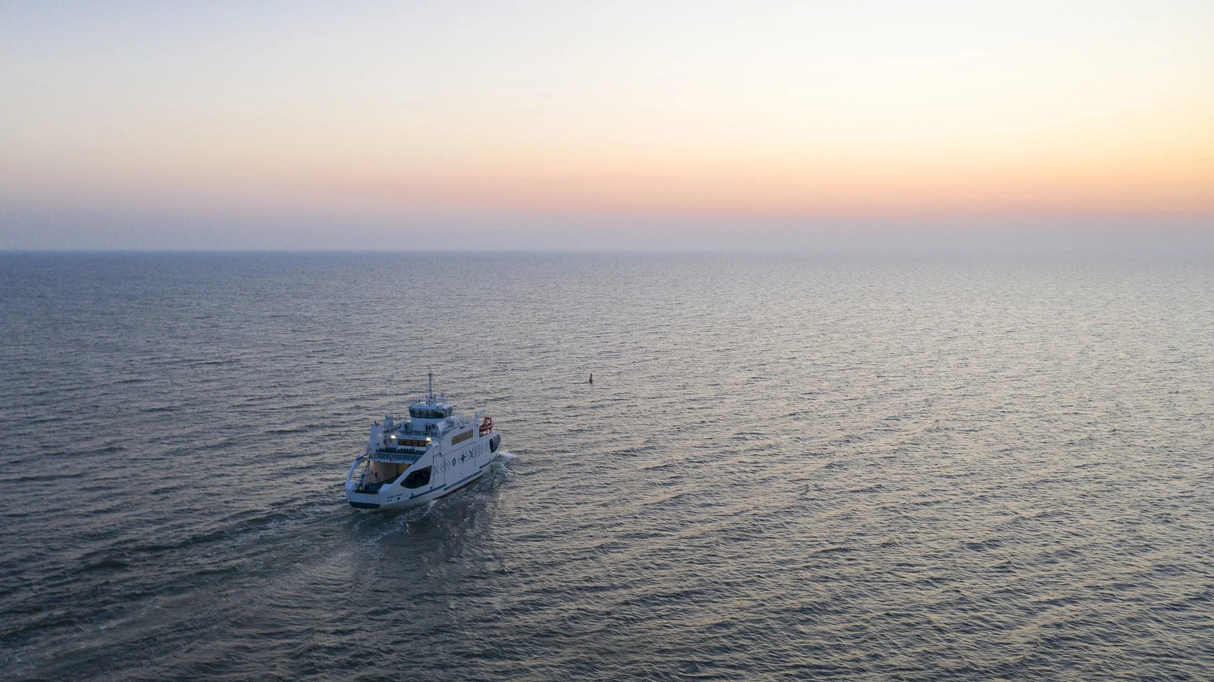 A white yacht sailing on calm ocean waters during sunset with a pastel sky in the background.