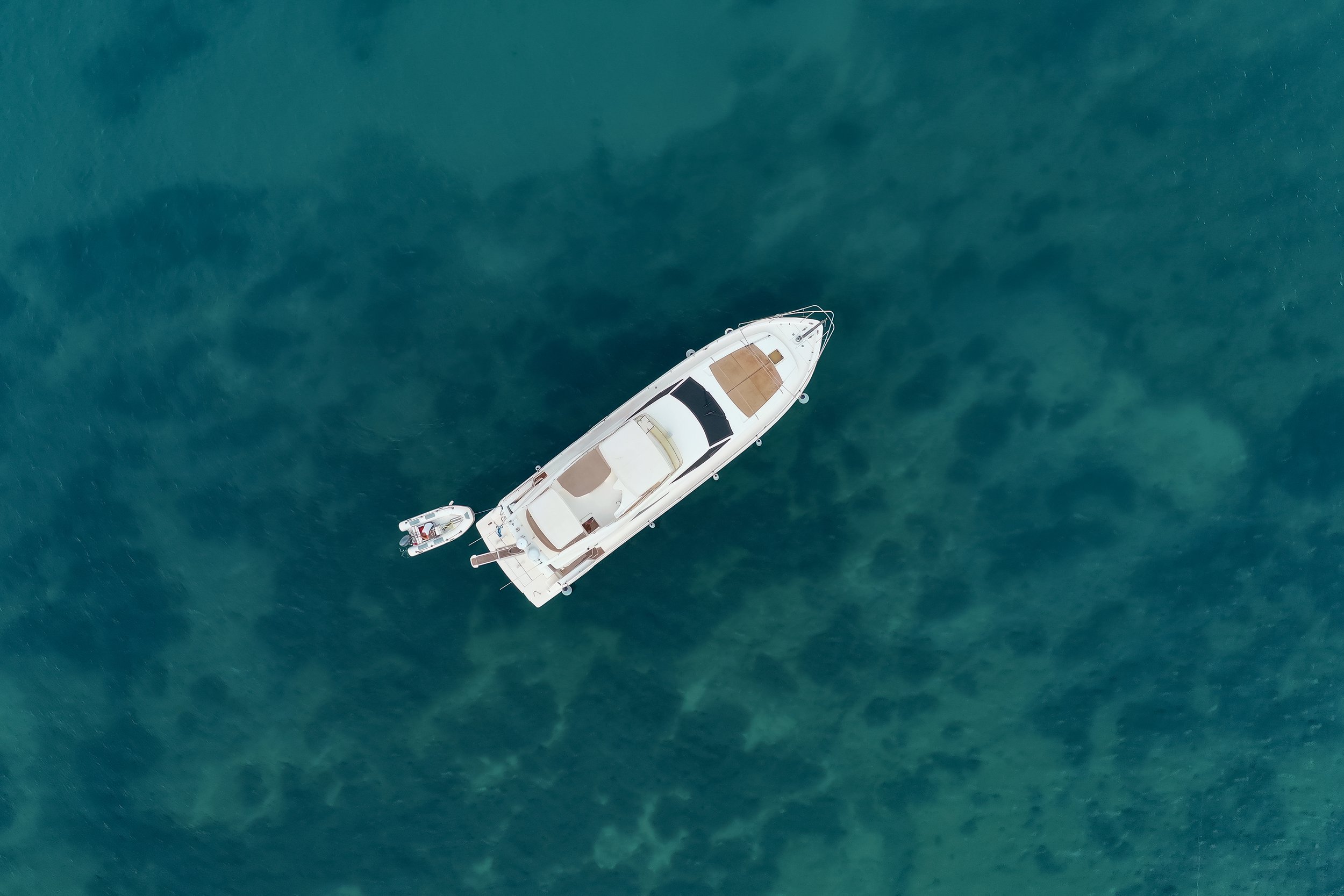 Overhead view of a white yacht floating on blue-green water.