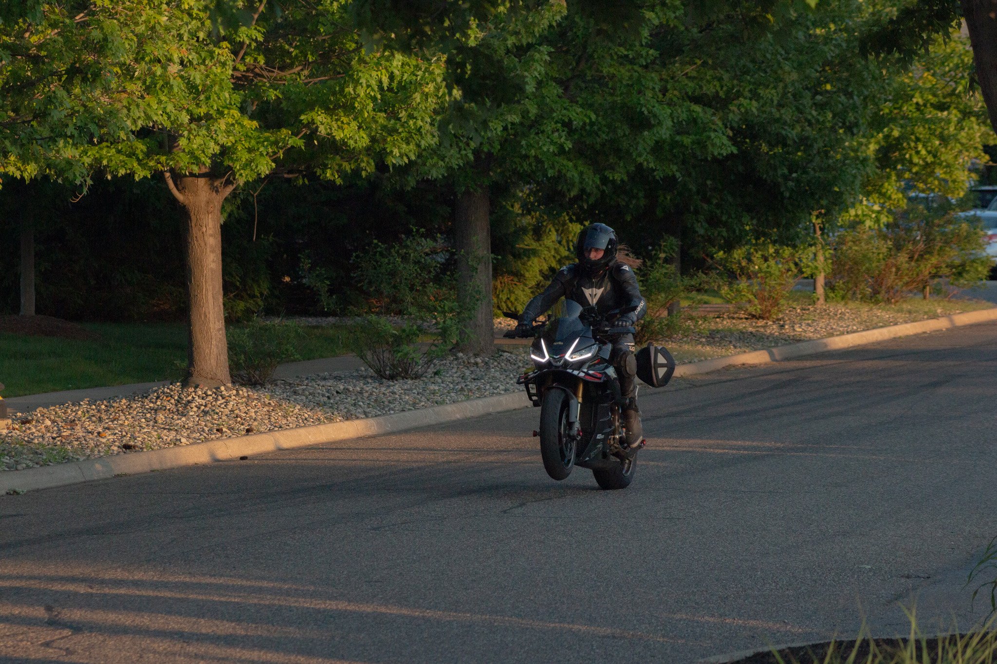 Motorcycle rider wearing a helmet and riding on a suburban street with trees and greenery.