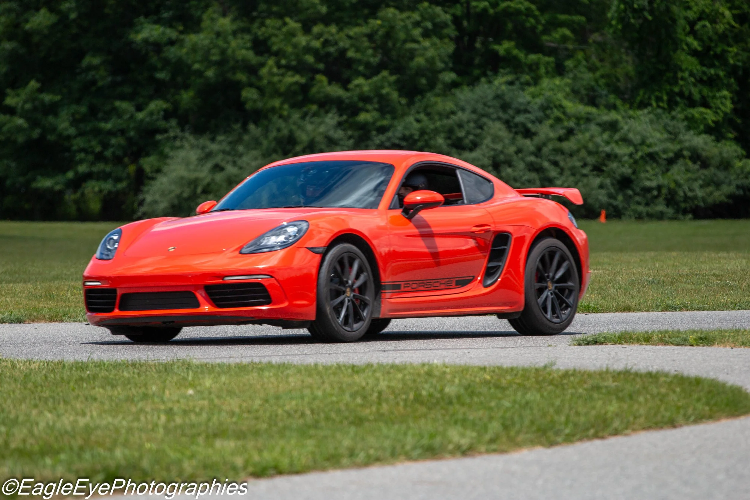 Red Porsche sports car driving on a grassy area with trees in the background.