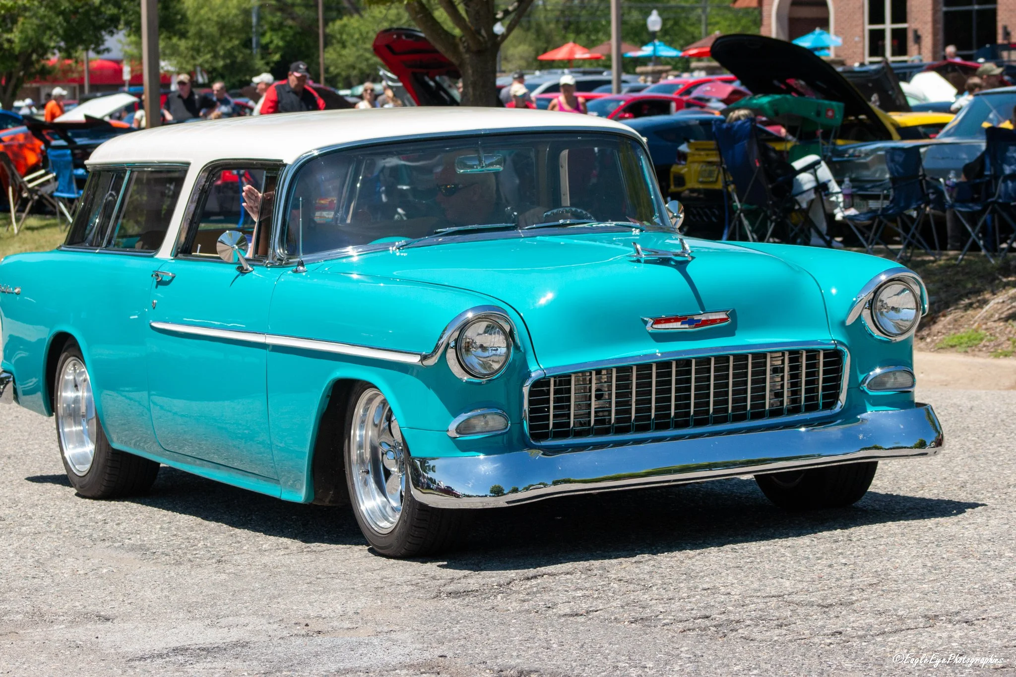 A vintage turquoise and white Chevrolet car at a classic car show with people and other cars in the background.