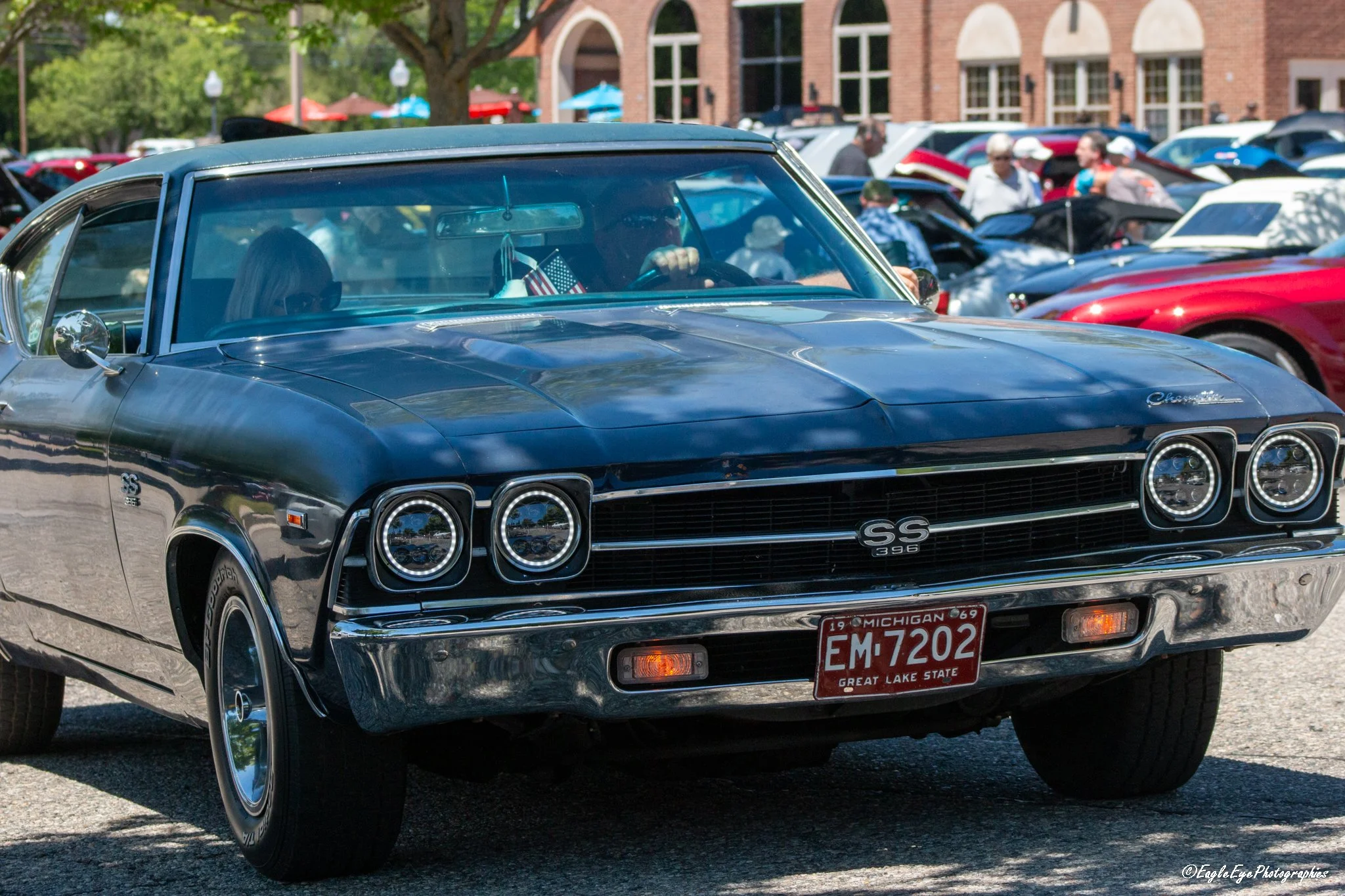 A classic black Chevrolet Chevelle SS 396 car at an outdoor car show with other vintage vehicles and people in the background.