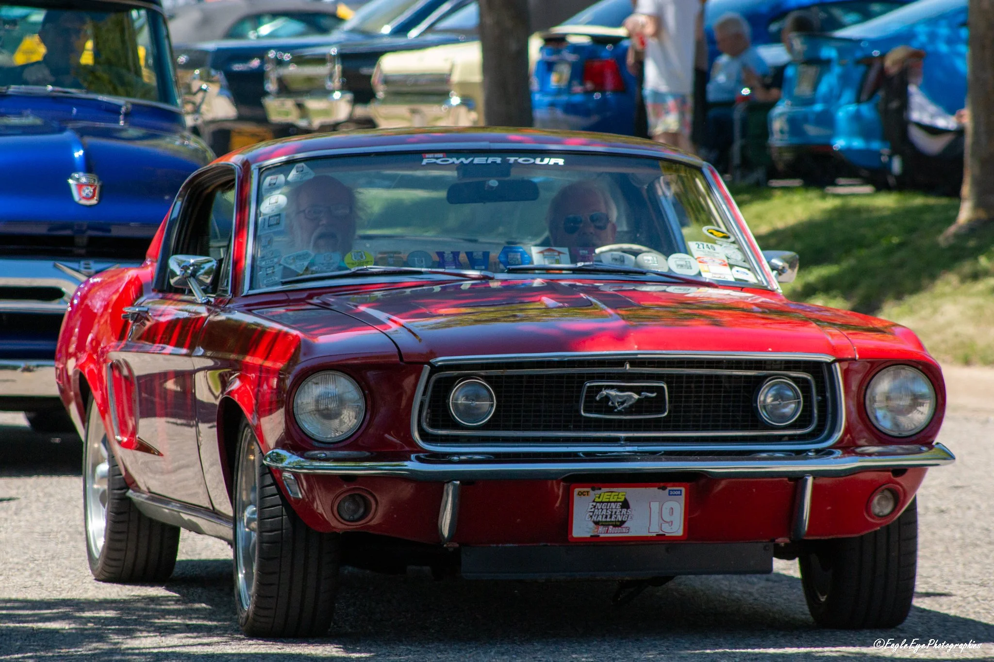 Red vintage Ford Mustang at a car show with people in the background.