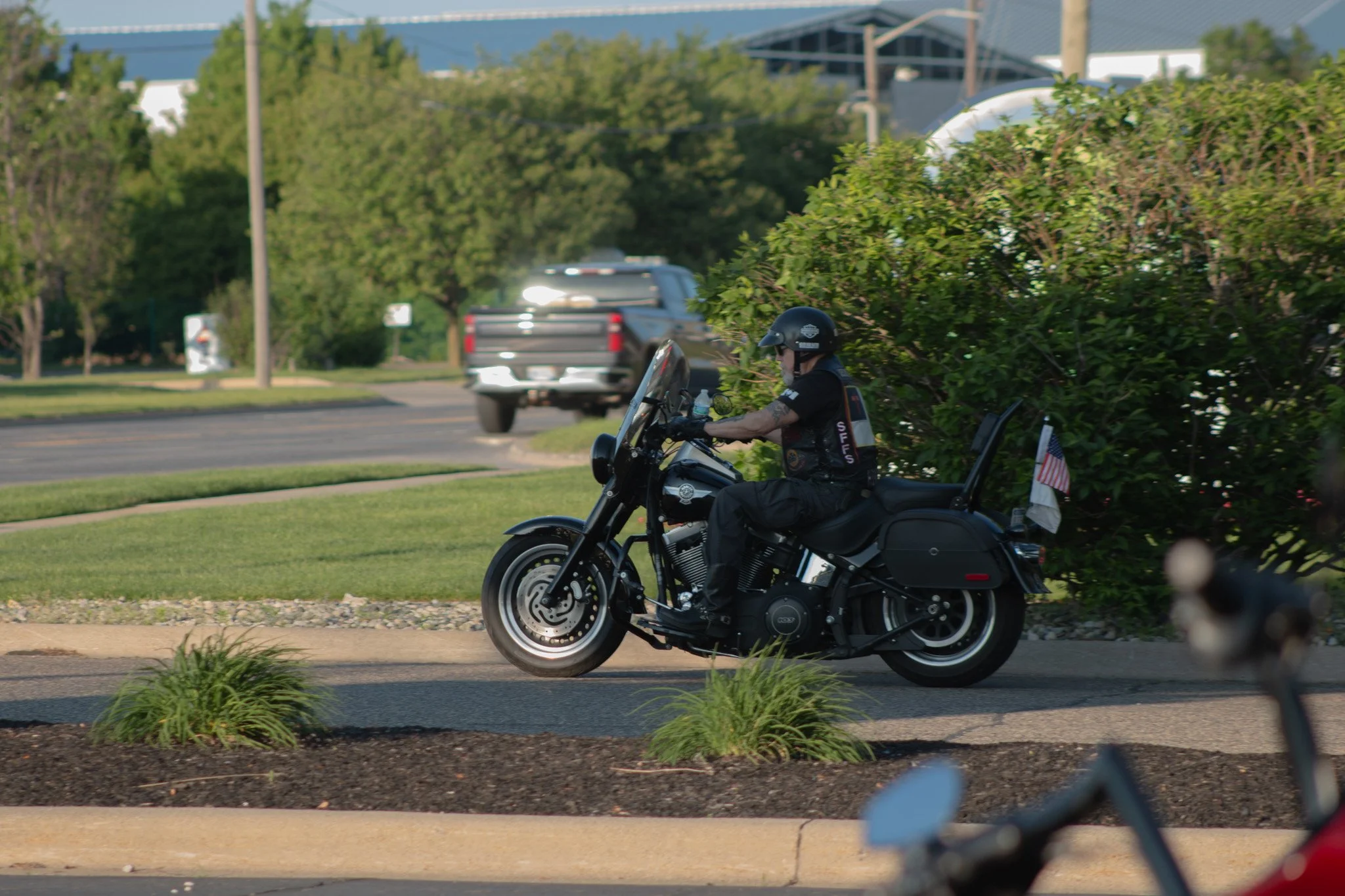 A person riding a black motorcycle on a city street with trees and buildings in the background.