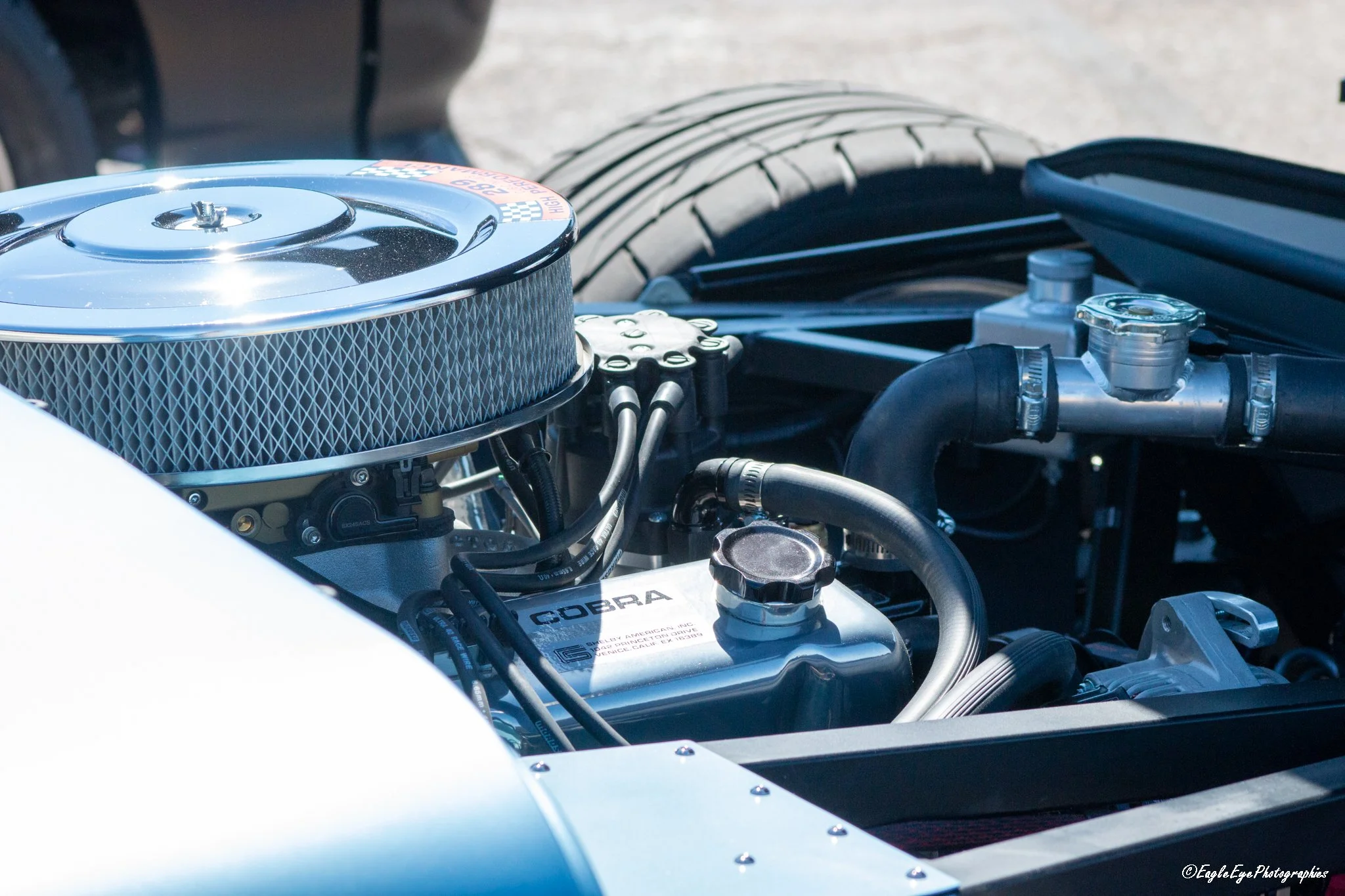 Close-up view of a car engine showing an air filter with a chrome top, connected hoses, and various engine components.