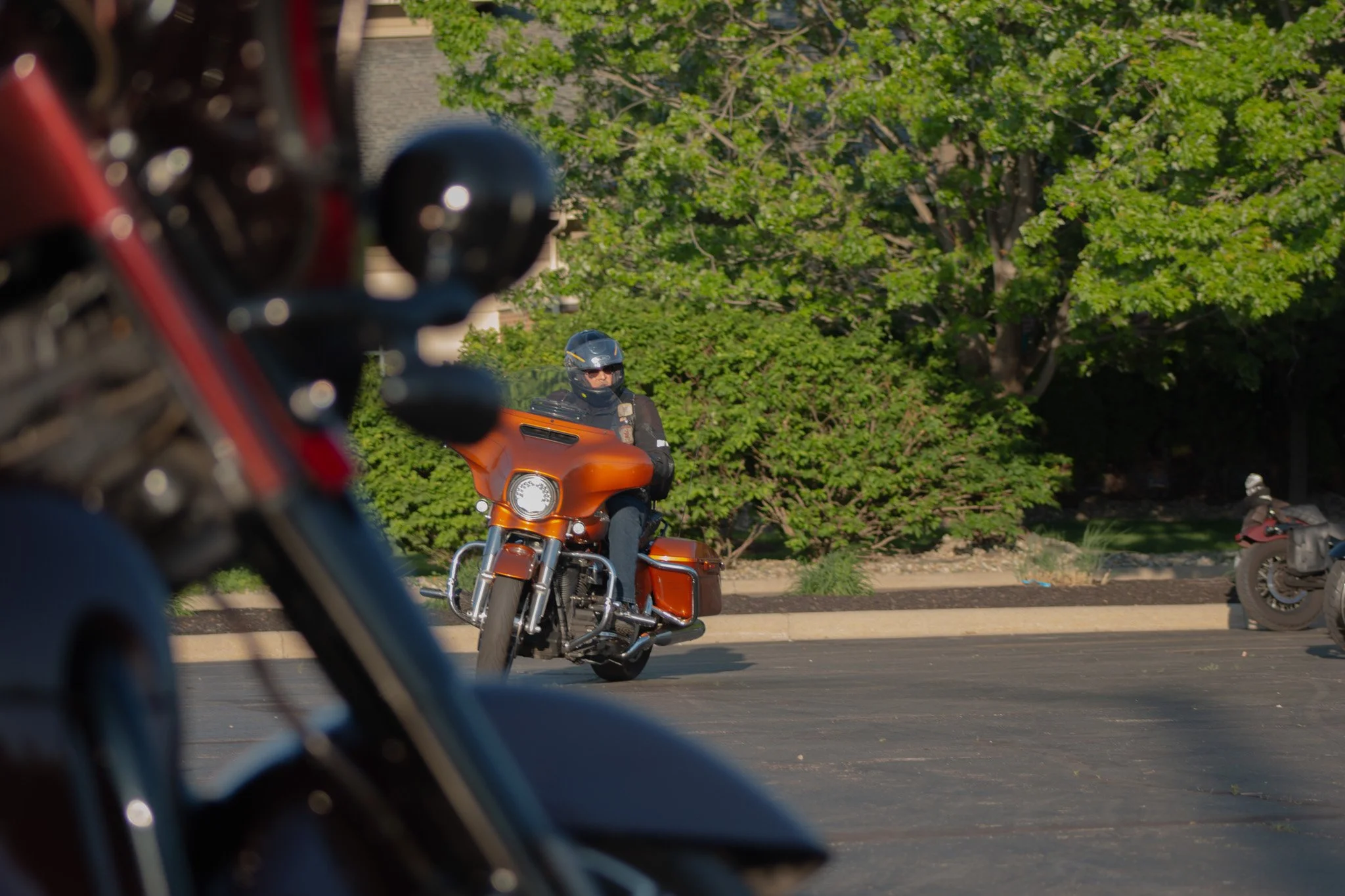 A motorcyclist wearing a helmet riding a motorcycle on the street with green trees in the background.