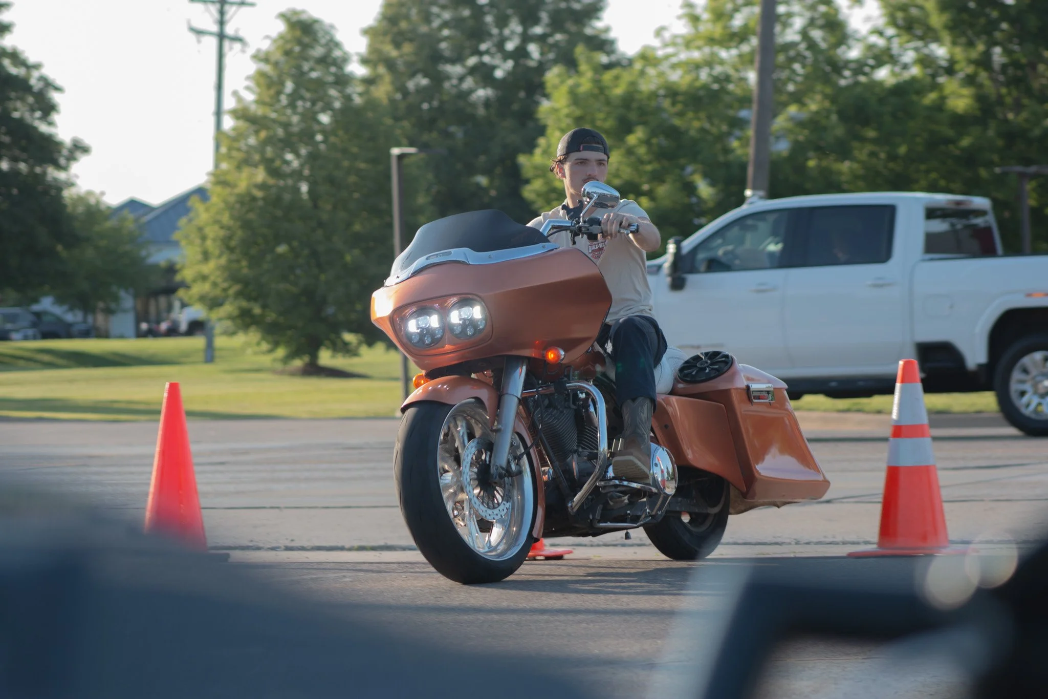 A man on a motorcycle navigating through orange traffic cones during a riding course or safety training session outdoors on a sunny day.