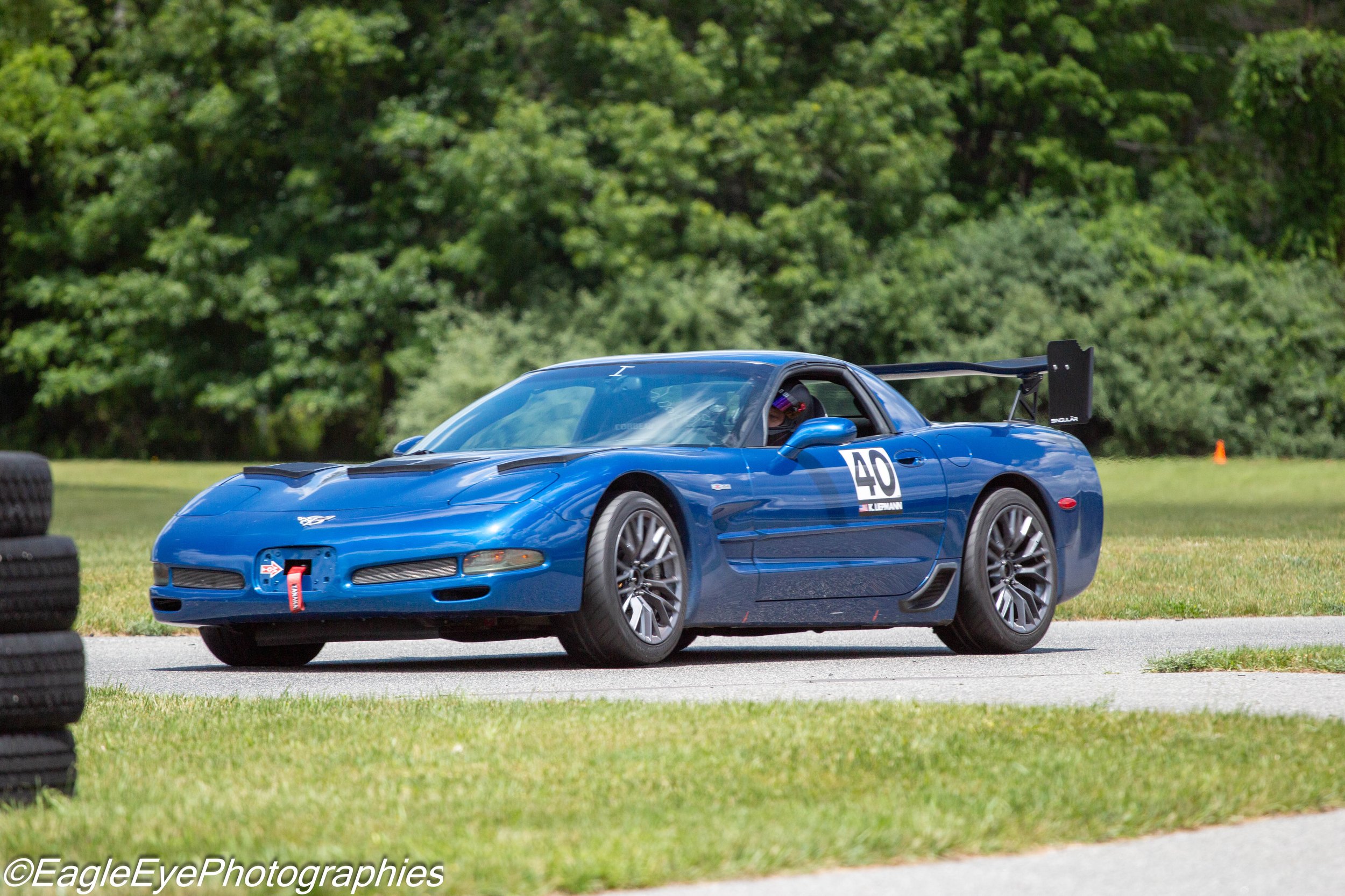A blue race car on a grassy field with green trees in the background. The car has the number 40 on its side and a large rear wing.