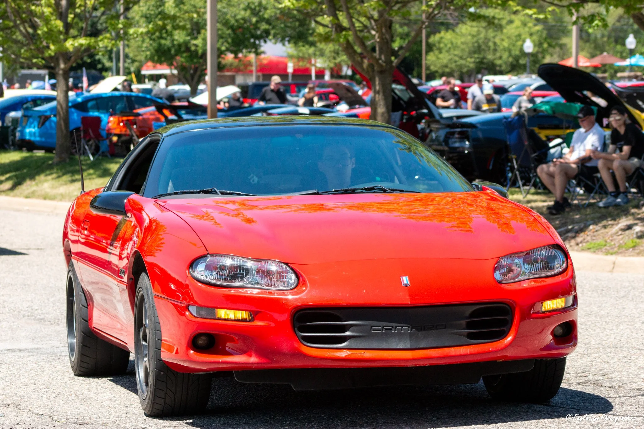 Red Chevrolet Camaro car at a car show with people in the background.